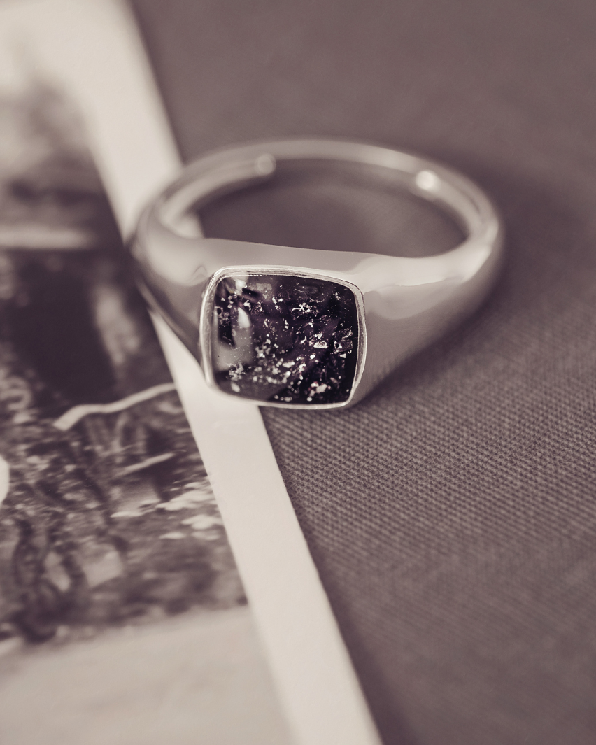 Silver ring with a dark stone on a textured surface