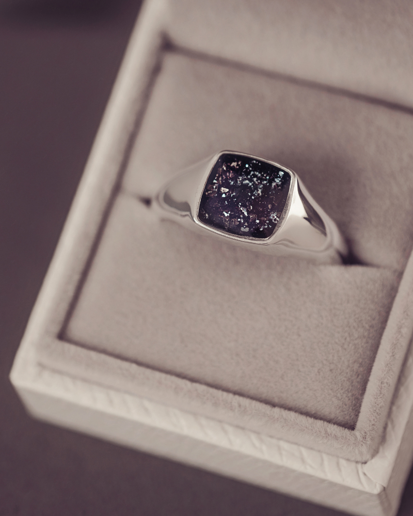 Silver ring with a dark stone in a jewelry box on a purple background