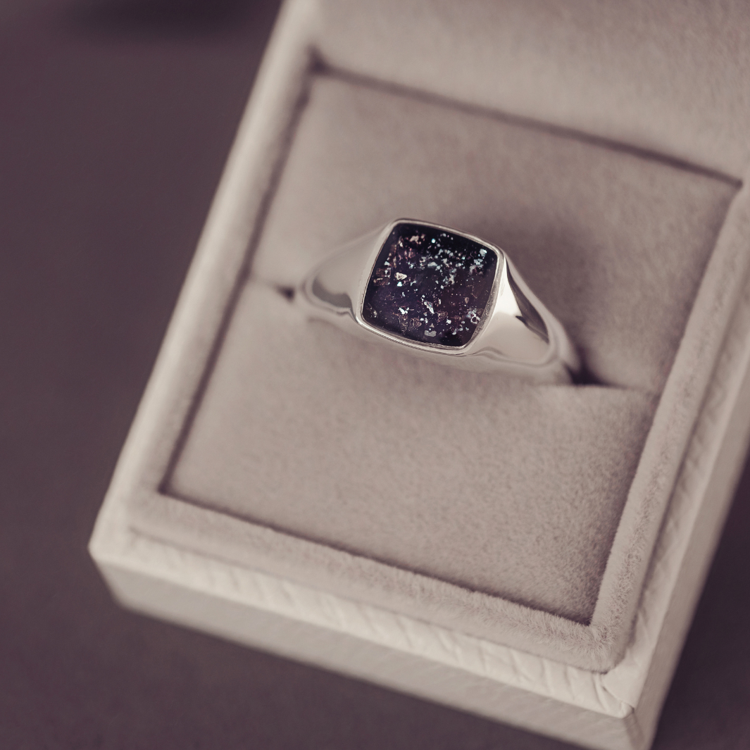 Silver ring with a dark stone in a jewelry box on a purple background