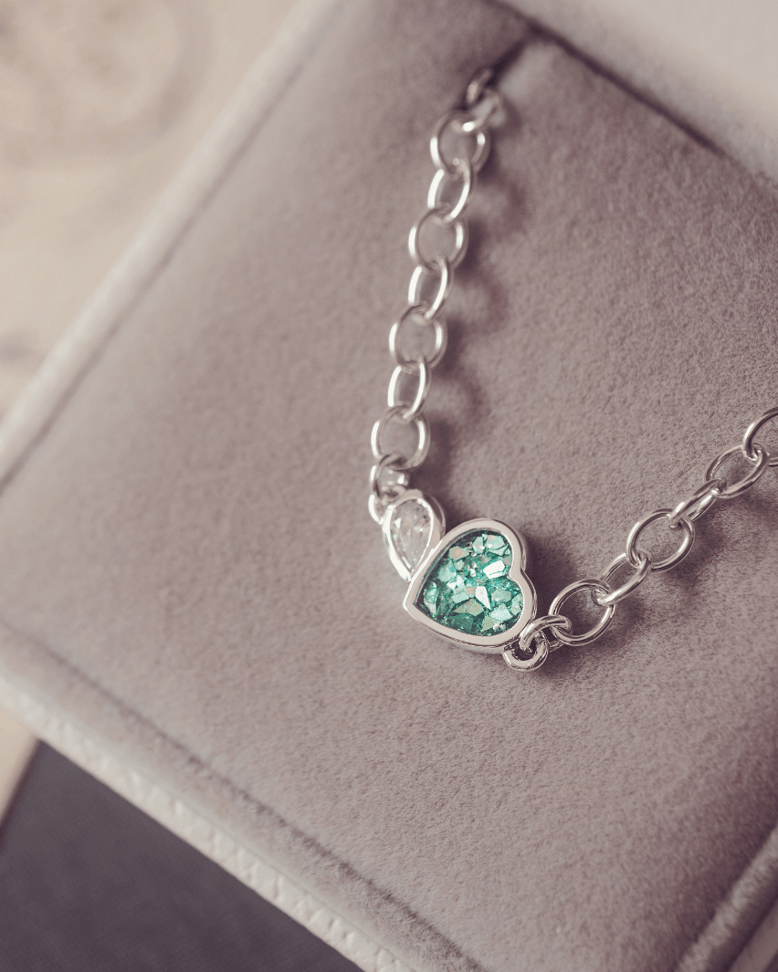 Silver bracelet with a heart-shaped green gemstone on a soft gray background