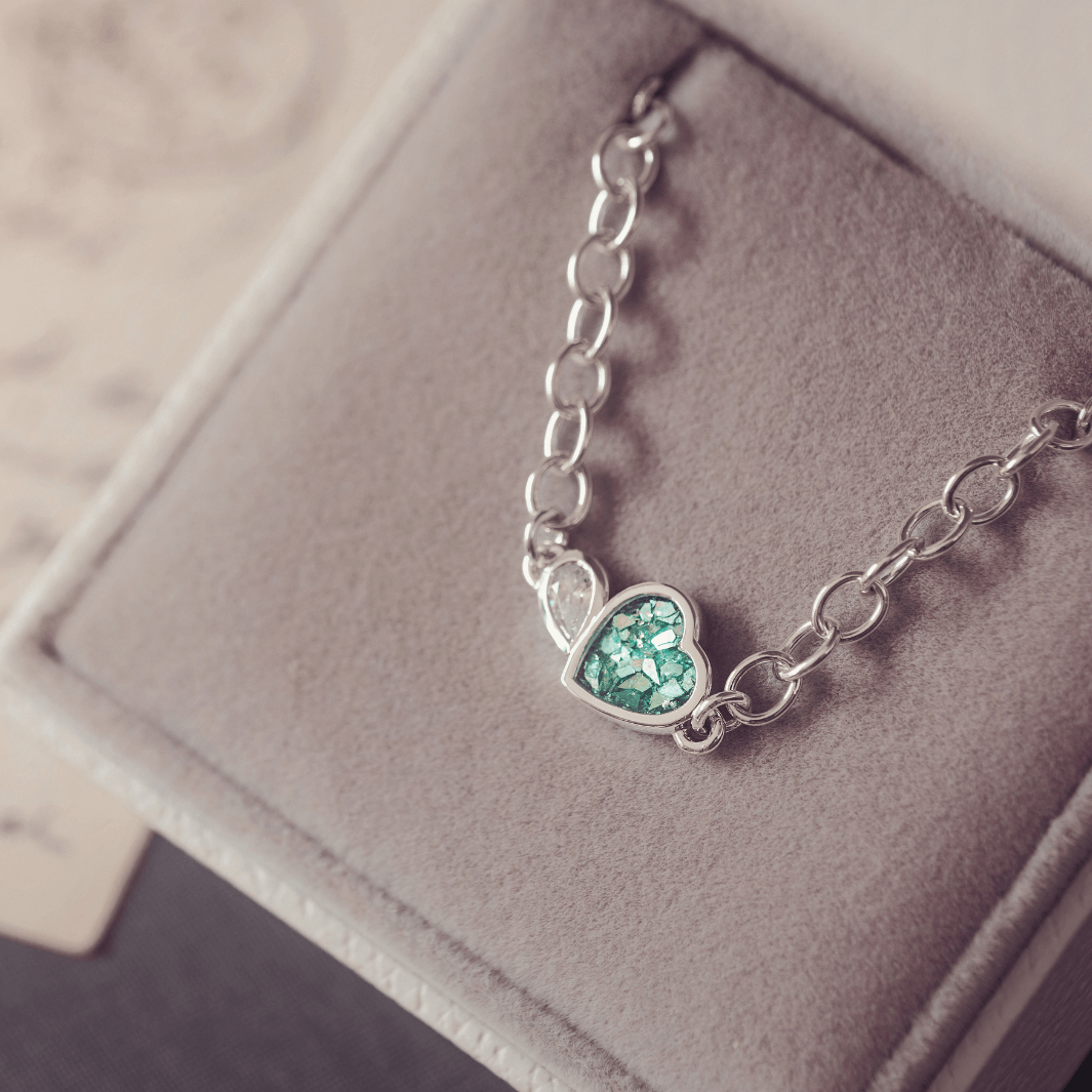 Silver bracelet with a heart-shaped green gemstone on a soft gray background