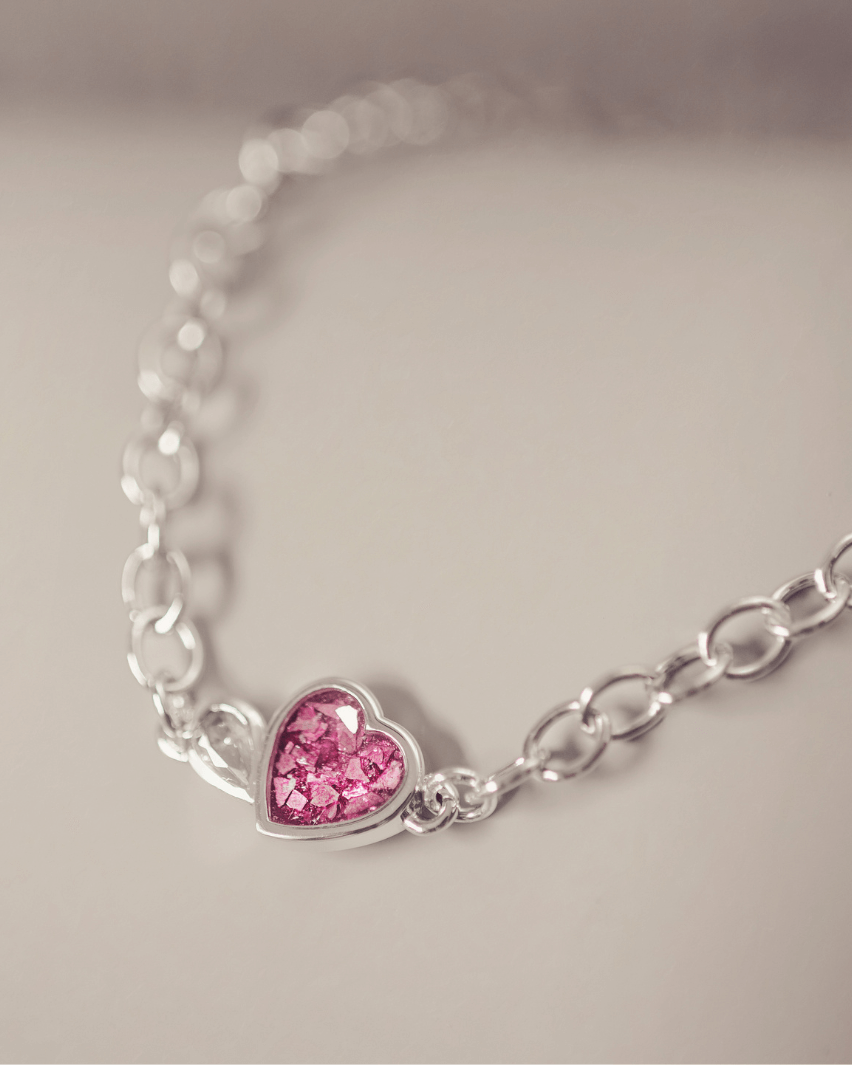 Silver bracelet with a pink heart-shaped charm on a light gray background