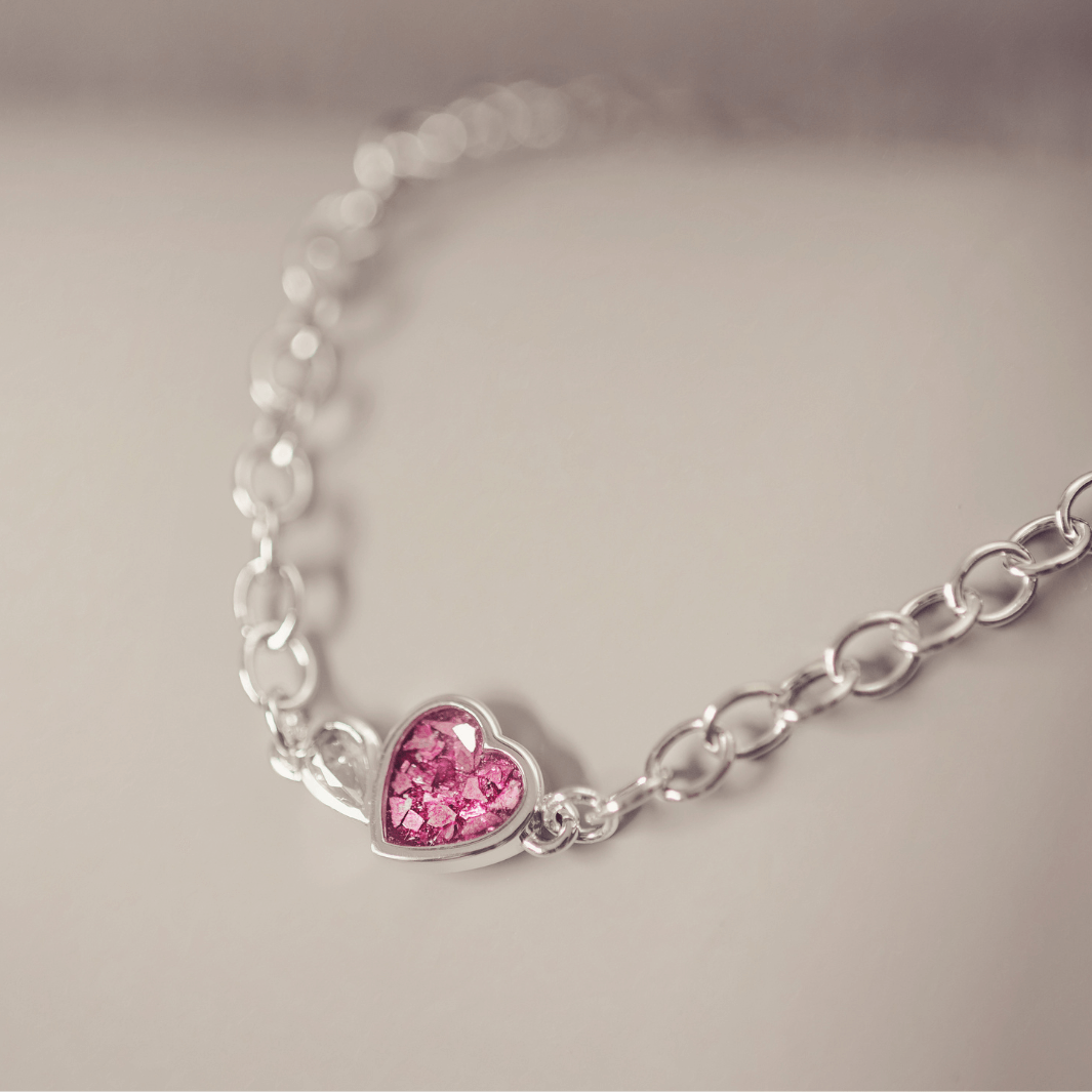 Silver bracelet with a pink heart-shaped charm on a light gray background