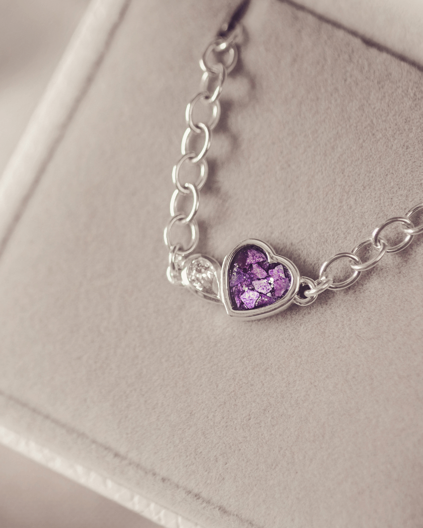 Silver bracelet with a heart-shaped purple gemstone on a light gray background
