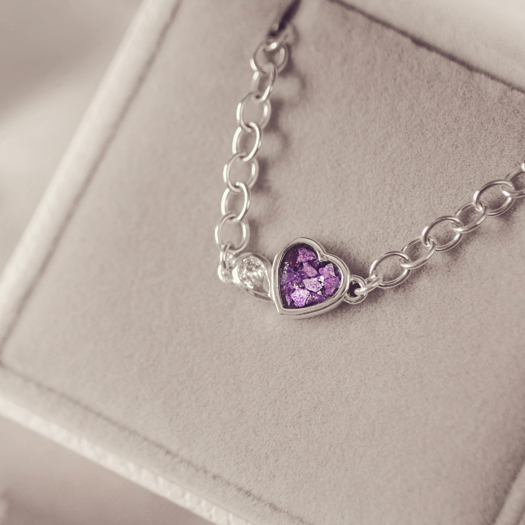 Silver bracelet with a heart-shaped purple gemstone on a light gray background