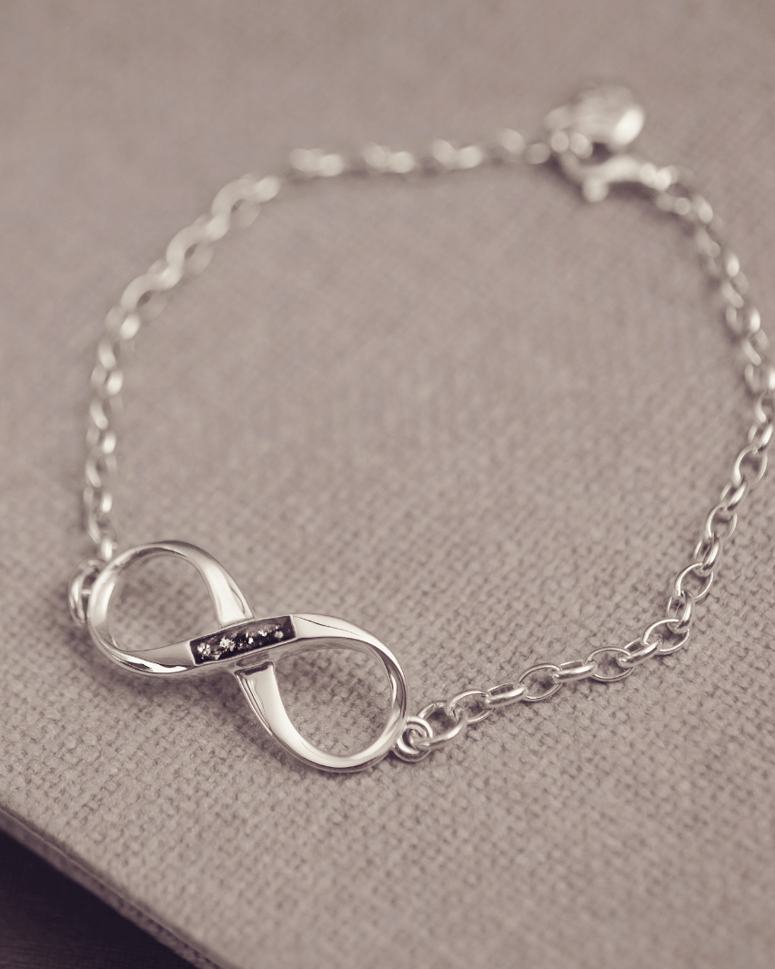 Silver infinity bracelet on a textured surface, includes cremation ashes set in black resin