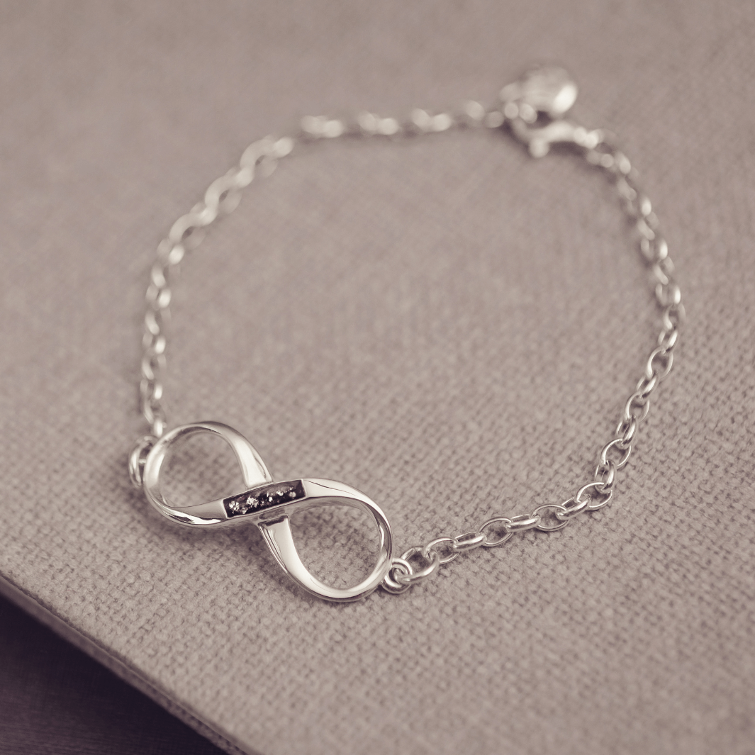 Silver infinity bracelet on a textured surface, includes cremation ashes set in black resin
