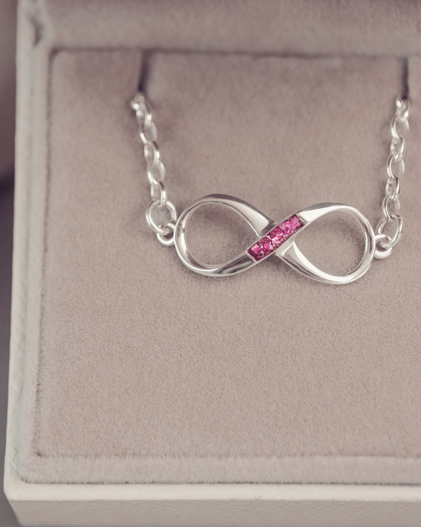 Silver infinity necklace with pink gemstones on a jewelry box