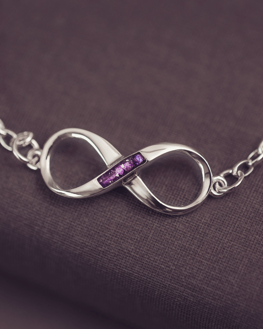 Silver infinity necklace with purple stones on a dark fabric background