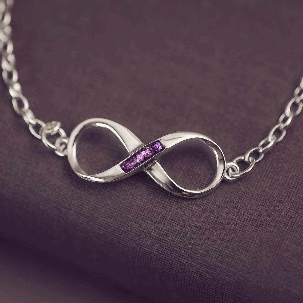 Silver infinity necklace with purple stones on a dark fabric background