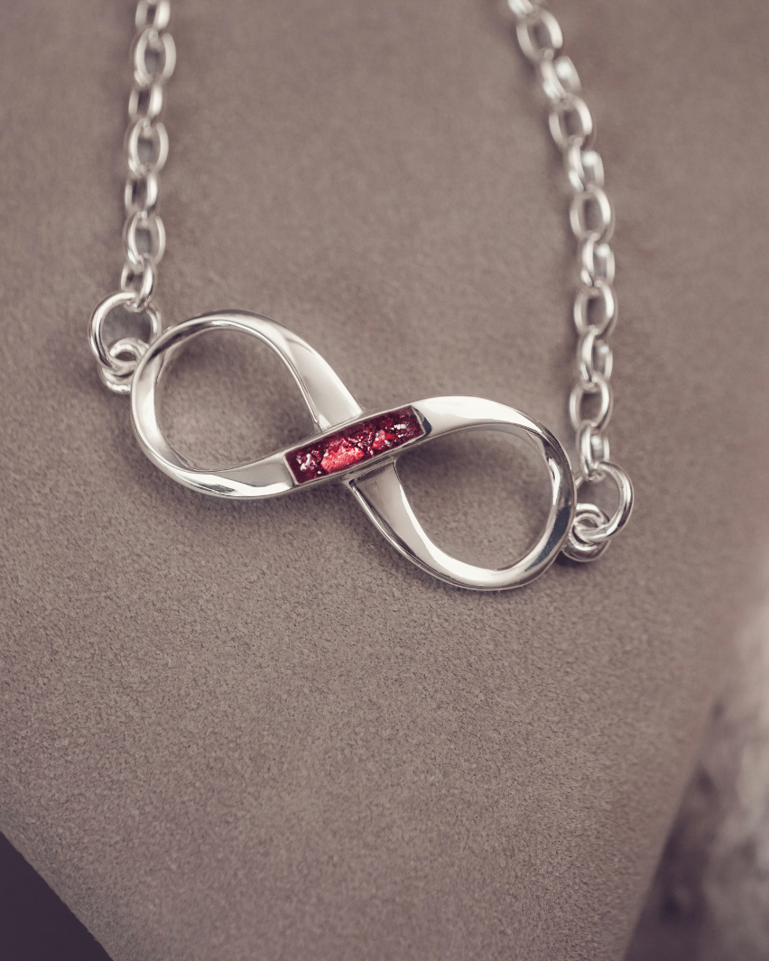Silver infinity necklace with a red gemstone on a neutral background