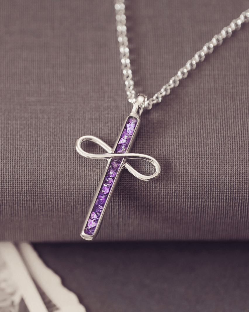 Silver cross necklace with purple stones on a textured surface