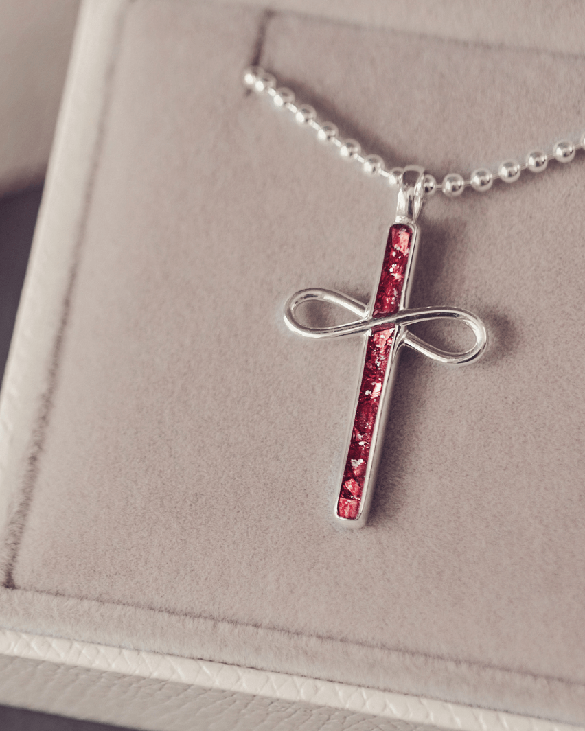 Silver cross pendant with red stones on a chain, displayed on a soft pink background