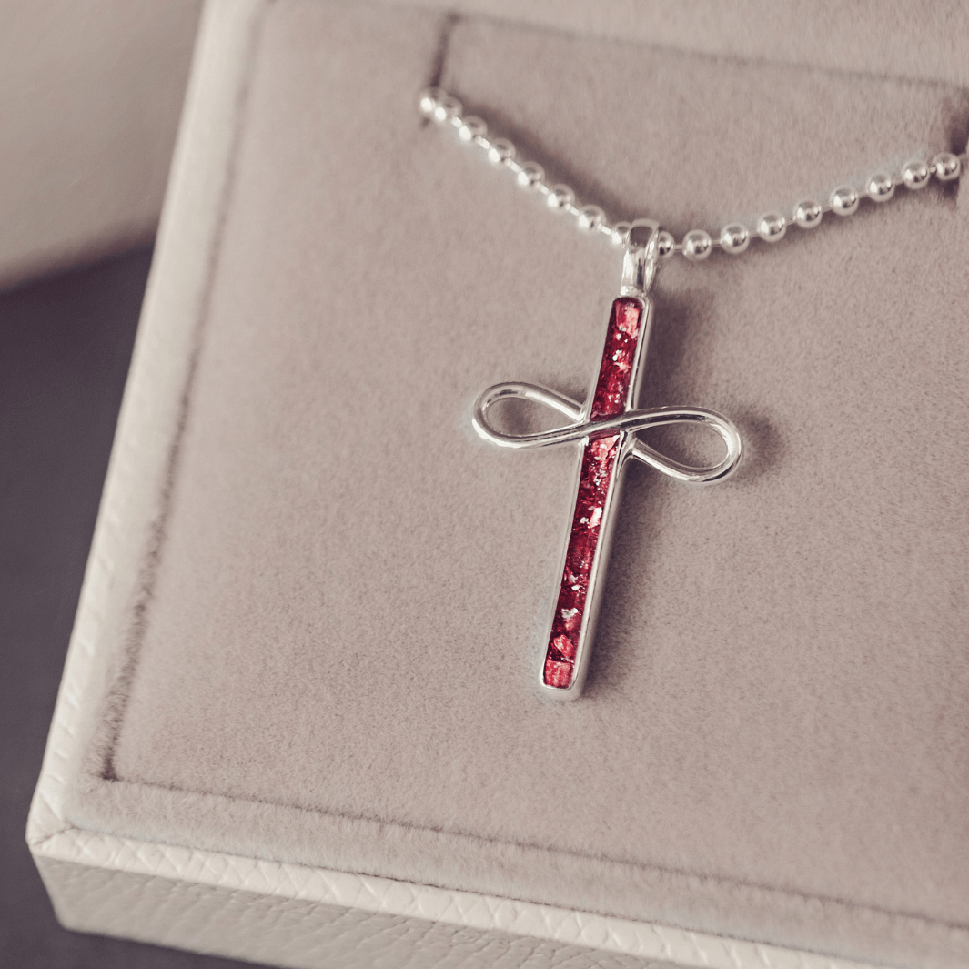 Silver cross pendant with red stones on a chain, displayed on a soft pink background