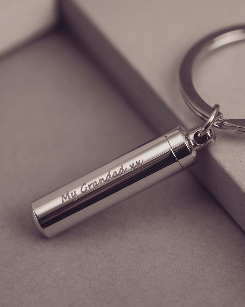 Cylindrical keyring which unscrews to hold cremation ashes or hair, engraved with the message "My Grandad xx" on one line, on a light grey background.