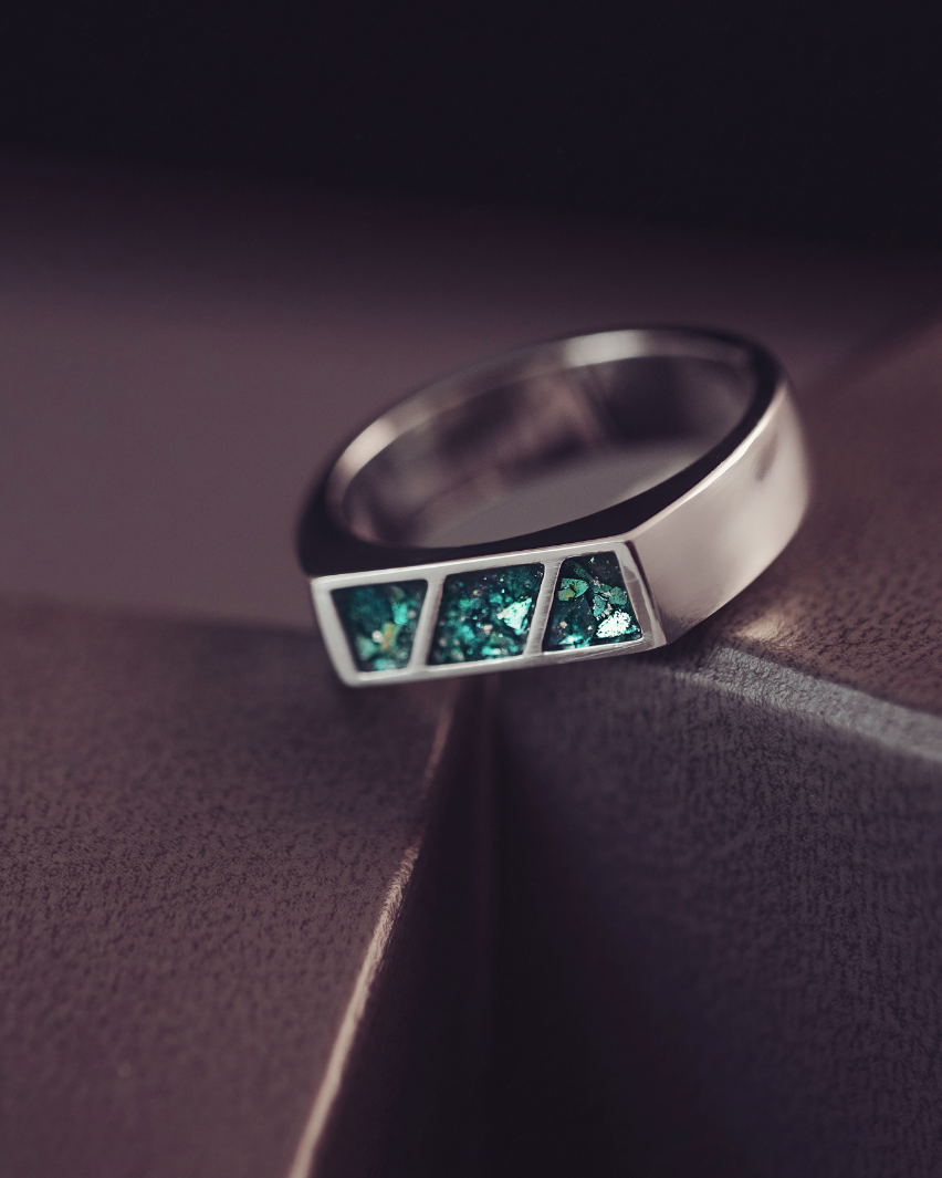 Silver ring with green gemstones on a dark surface