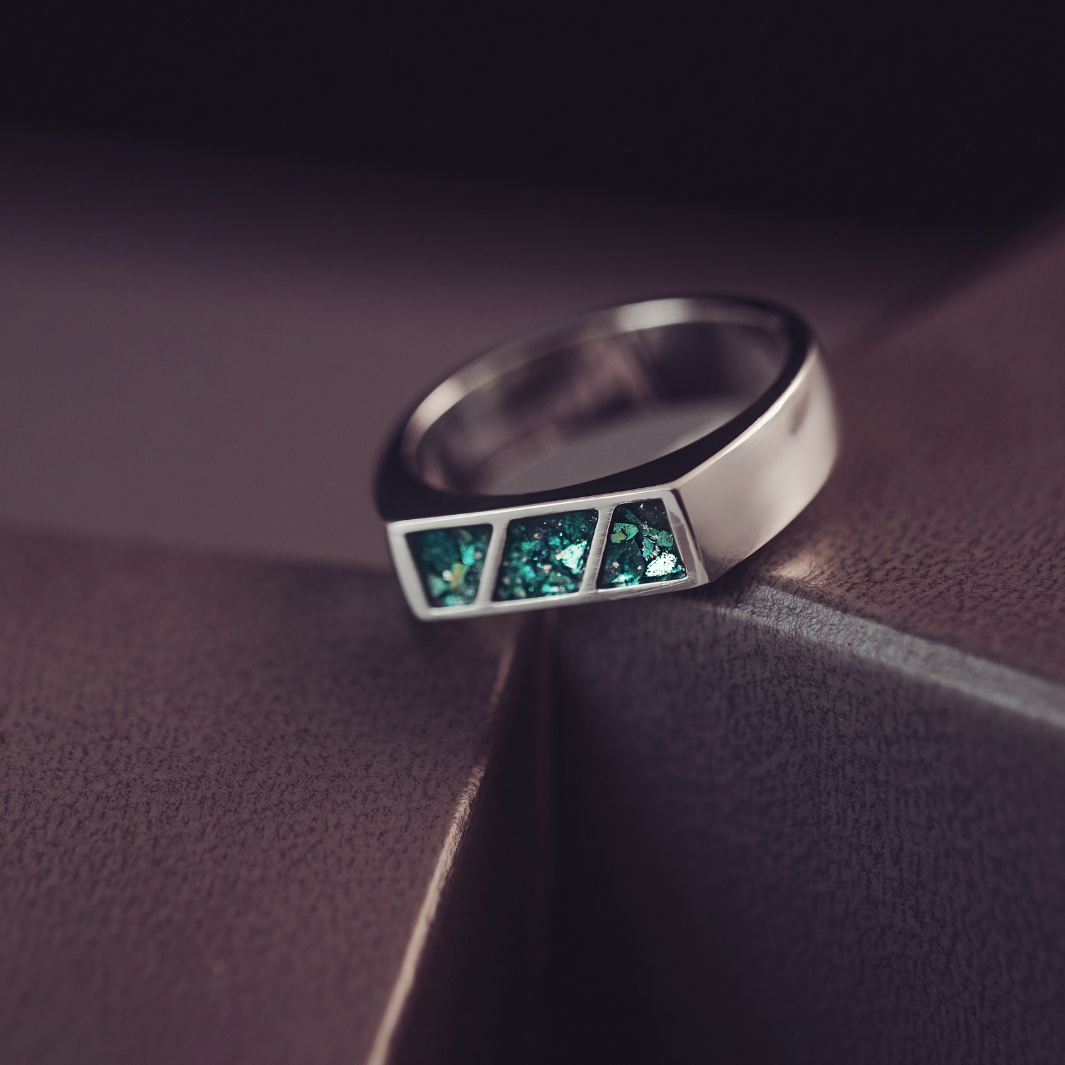 Silver ring with green gemstones on a dark surface