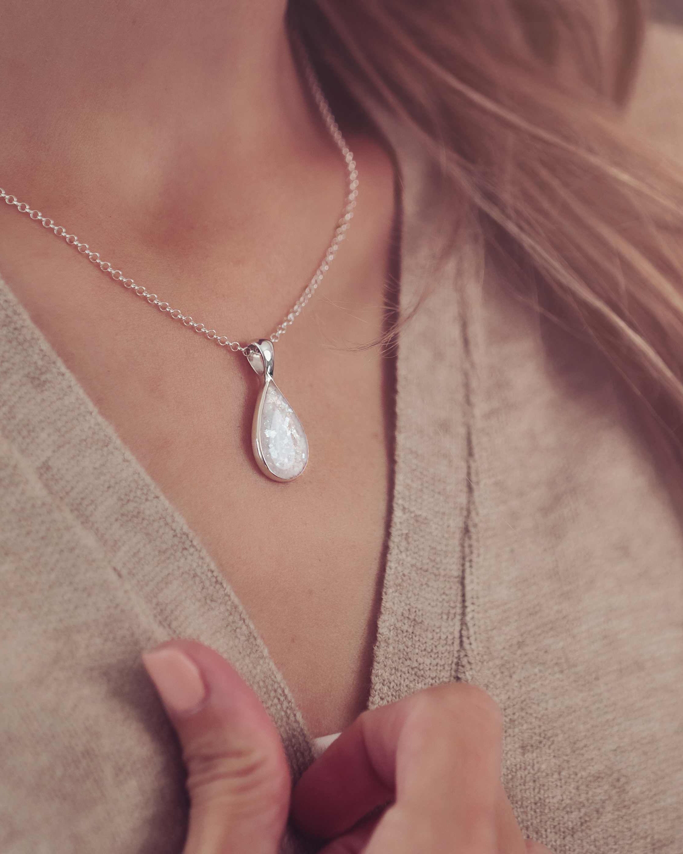Lady modelling a teardrop shaped necklace in a clear colour filled with Cremation Ashes