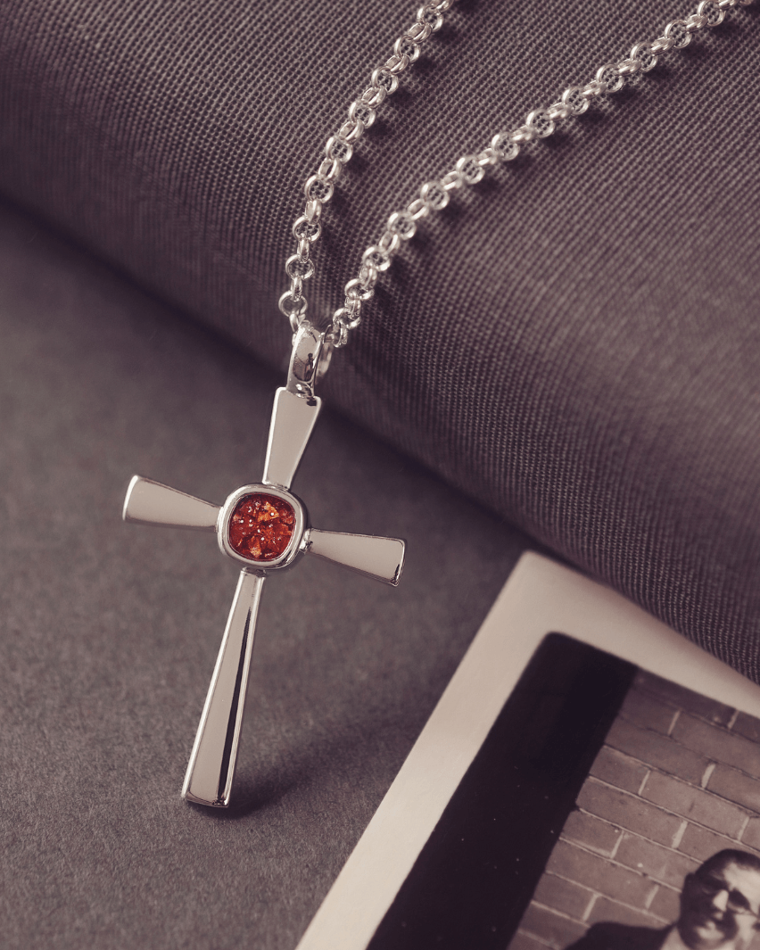 silver cross necklace with a section of resin and orange crystals, holding memorial ashes
