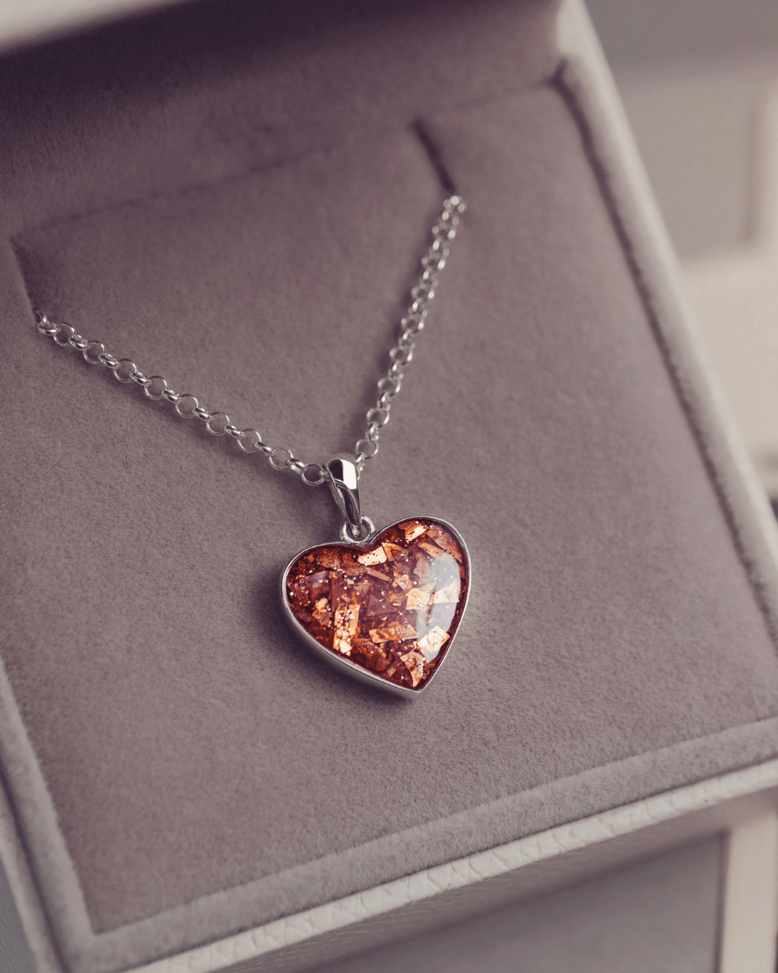 Sterling silver heart necklace with a central section filled with memorial ashes and orange crushed crystals, displayed in a grey jewellery box