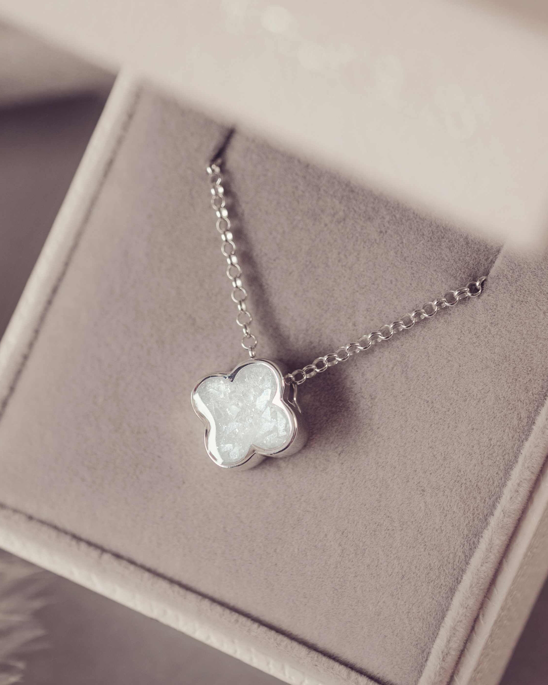 Silver necklace with a white clover-shaped pendant on a soft purple background