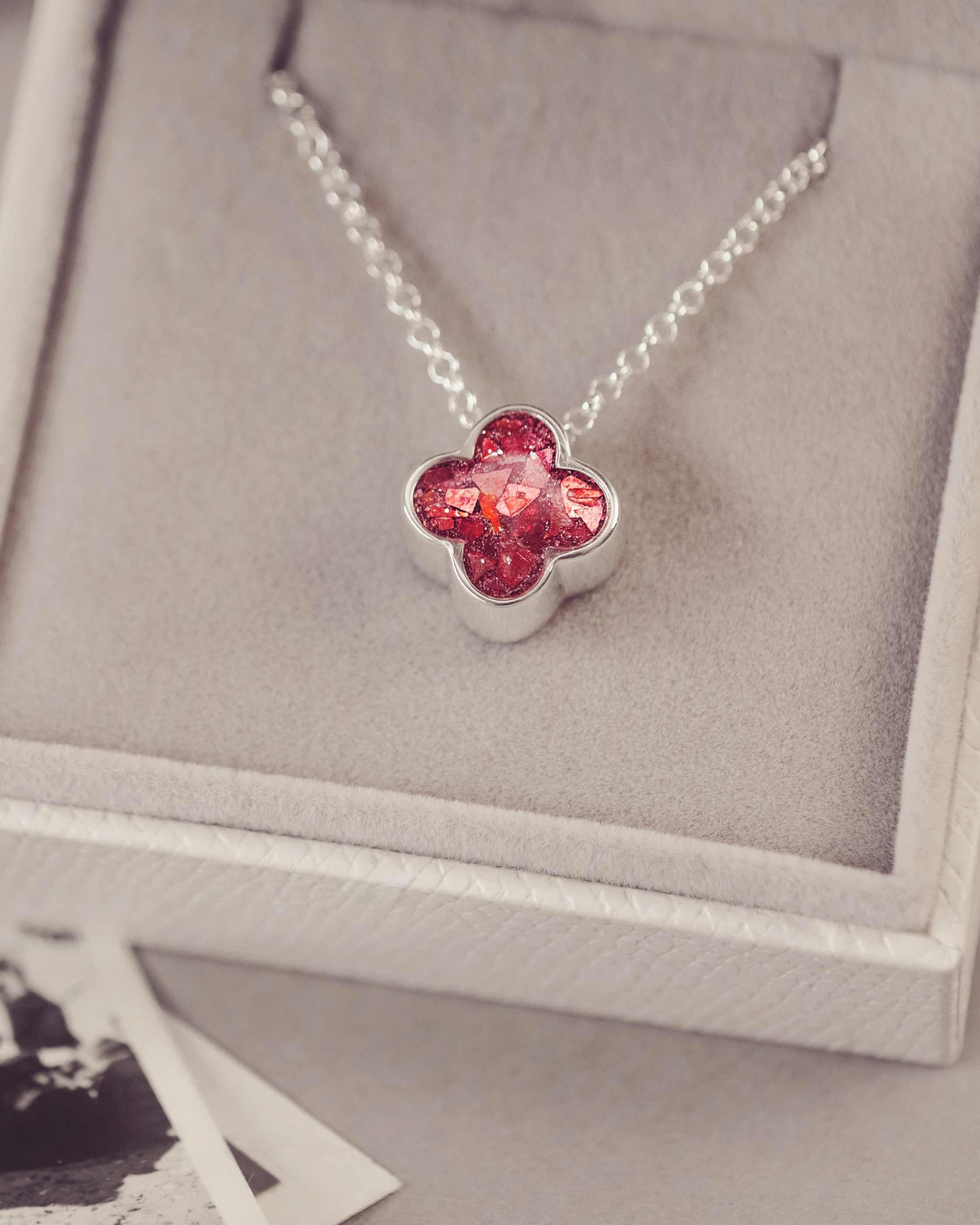 Necklace with a red clover-shaped pendant on a gray cushioned jewelry box.