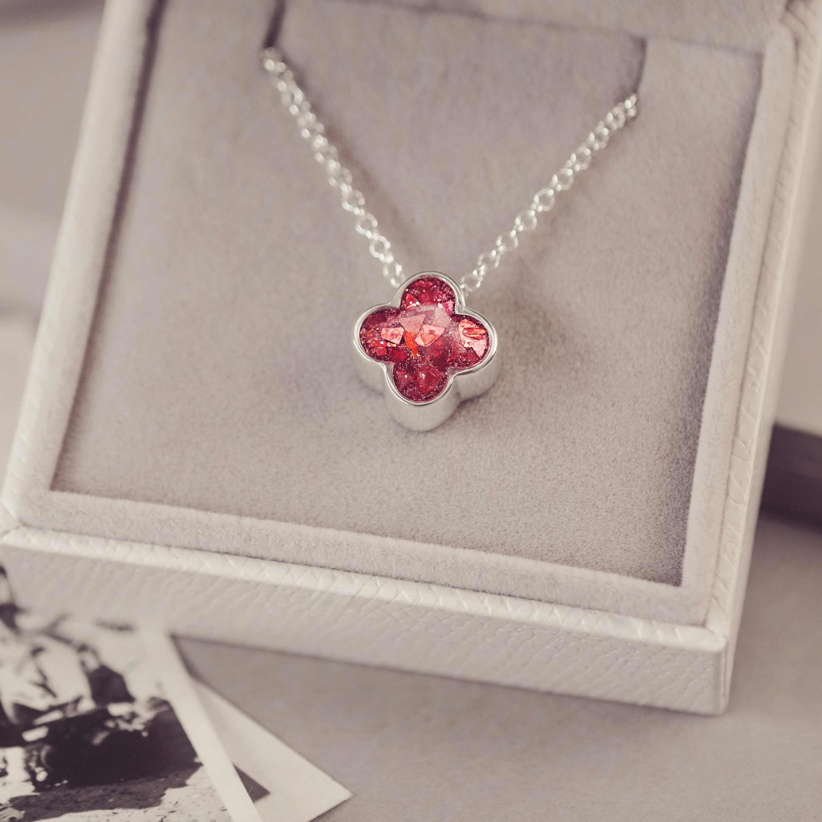 Necklace with a red clover-shaped pendant on a gray cushioned jewelry box.