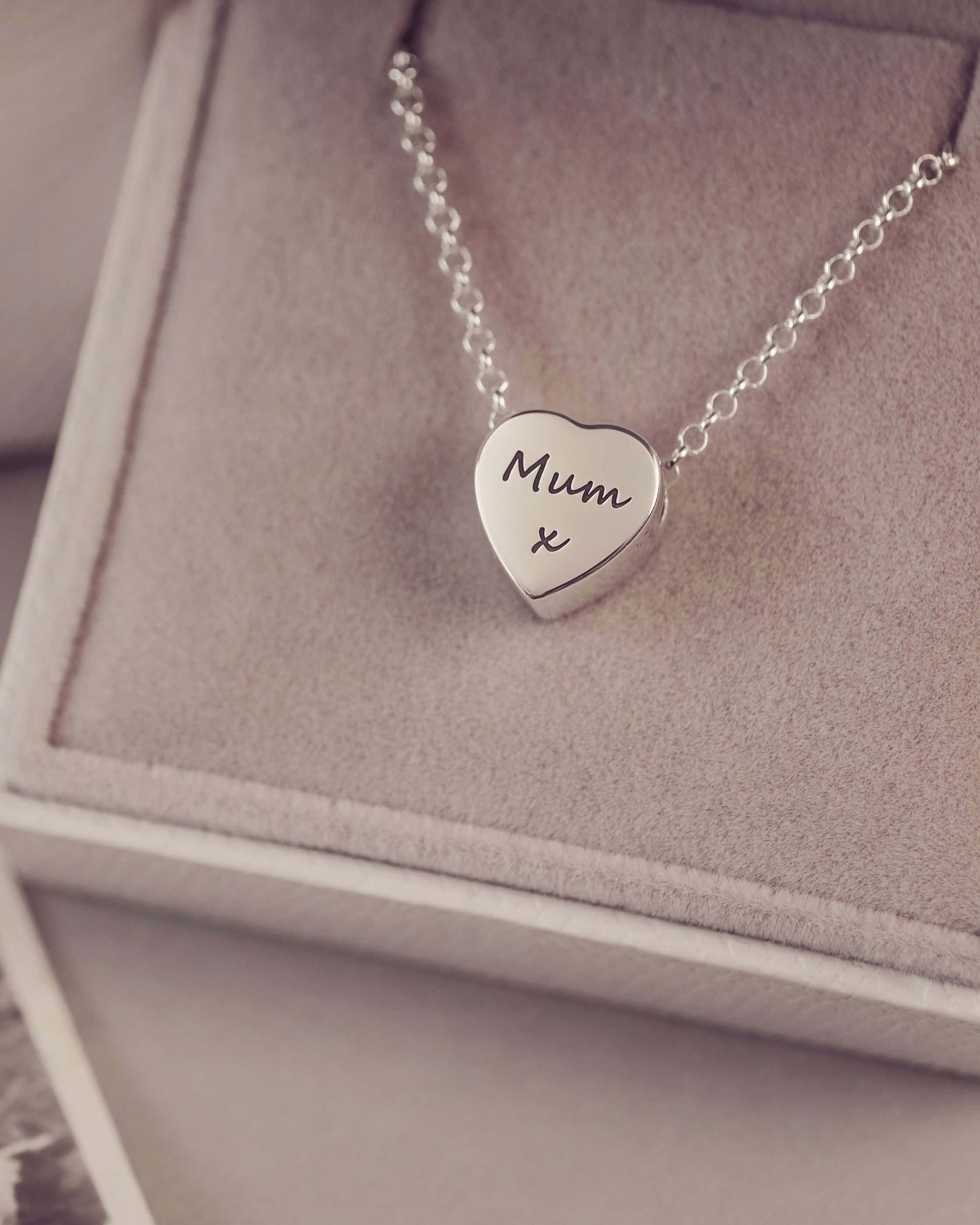 Silver heart-shaped necklace with 'Mum x' engraving on a textured surface