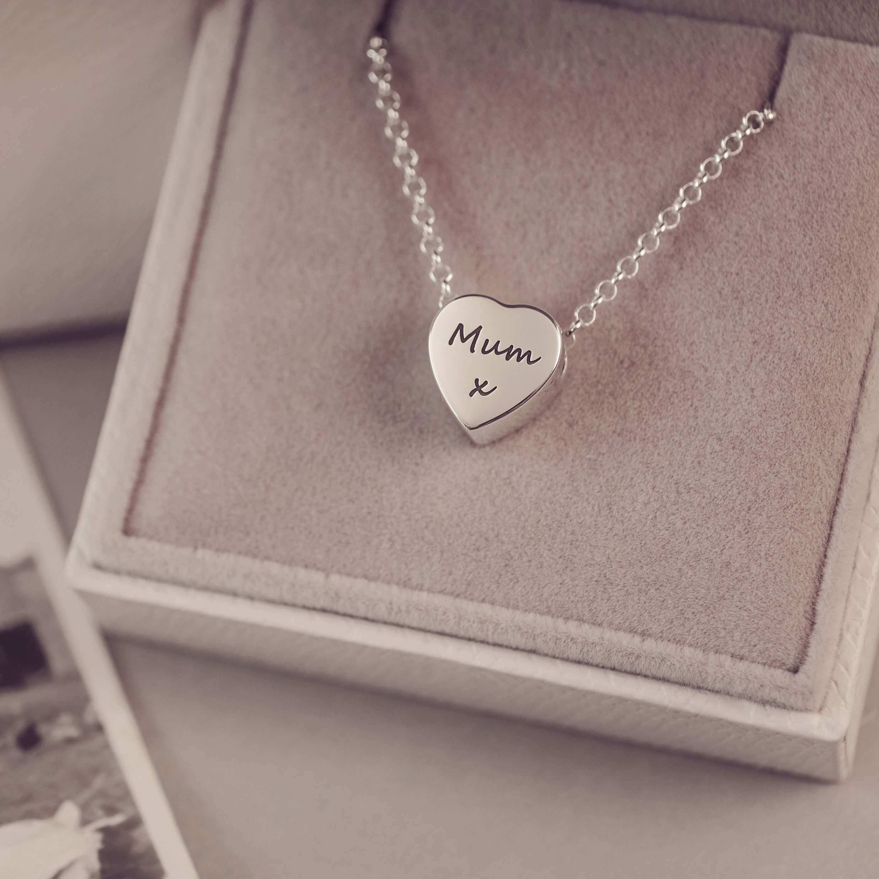 Silver heart-shaped necklace with 'Mum x' engraving on a textured surface