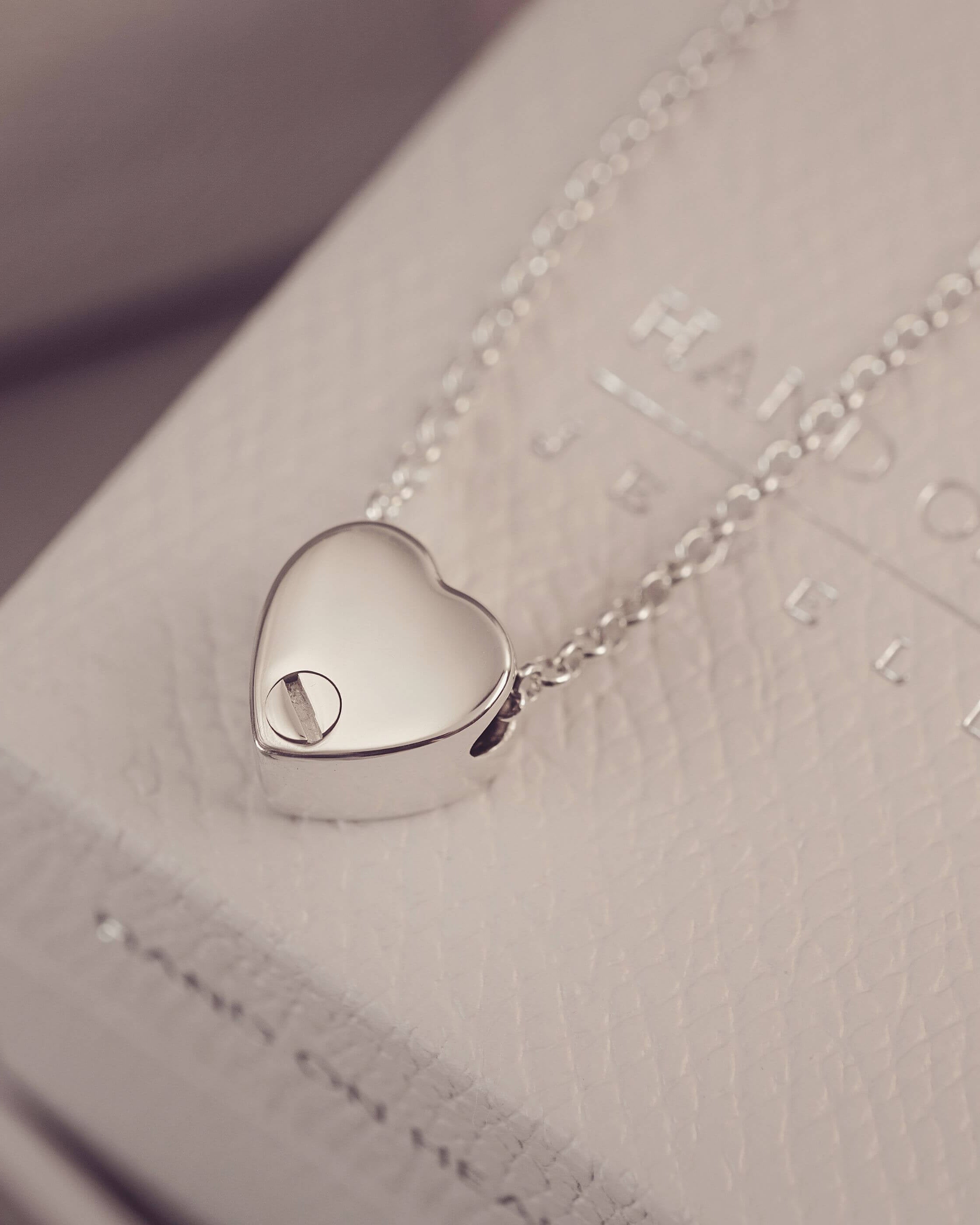Silver heart-shaped pendant on a chain against a textured surface
