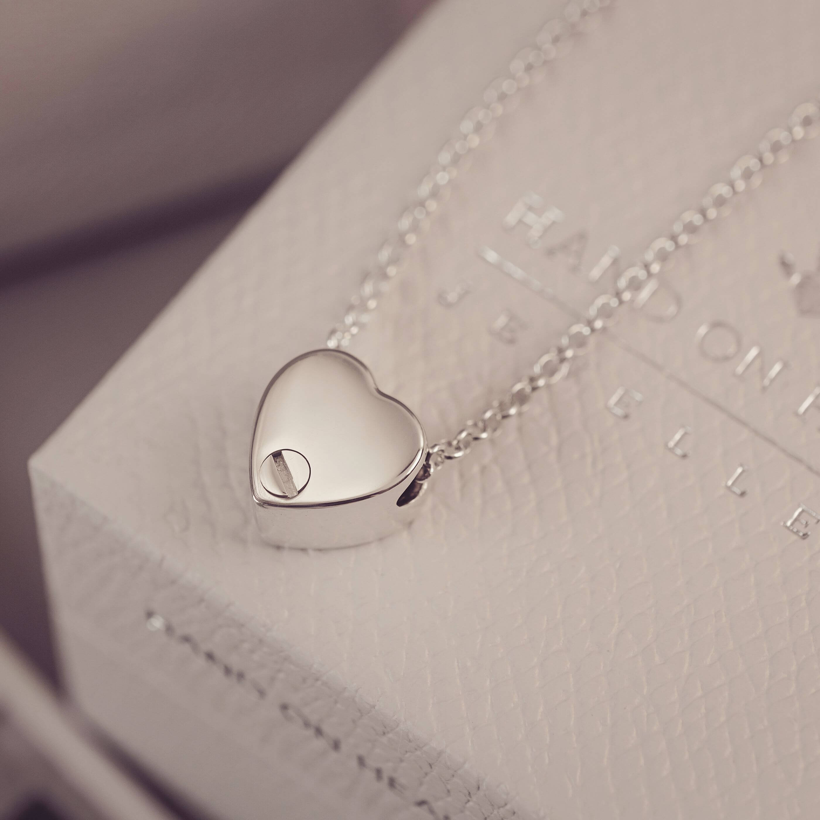 Silver heart-shaped pendant on a chain against a textured surface