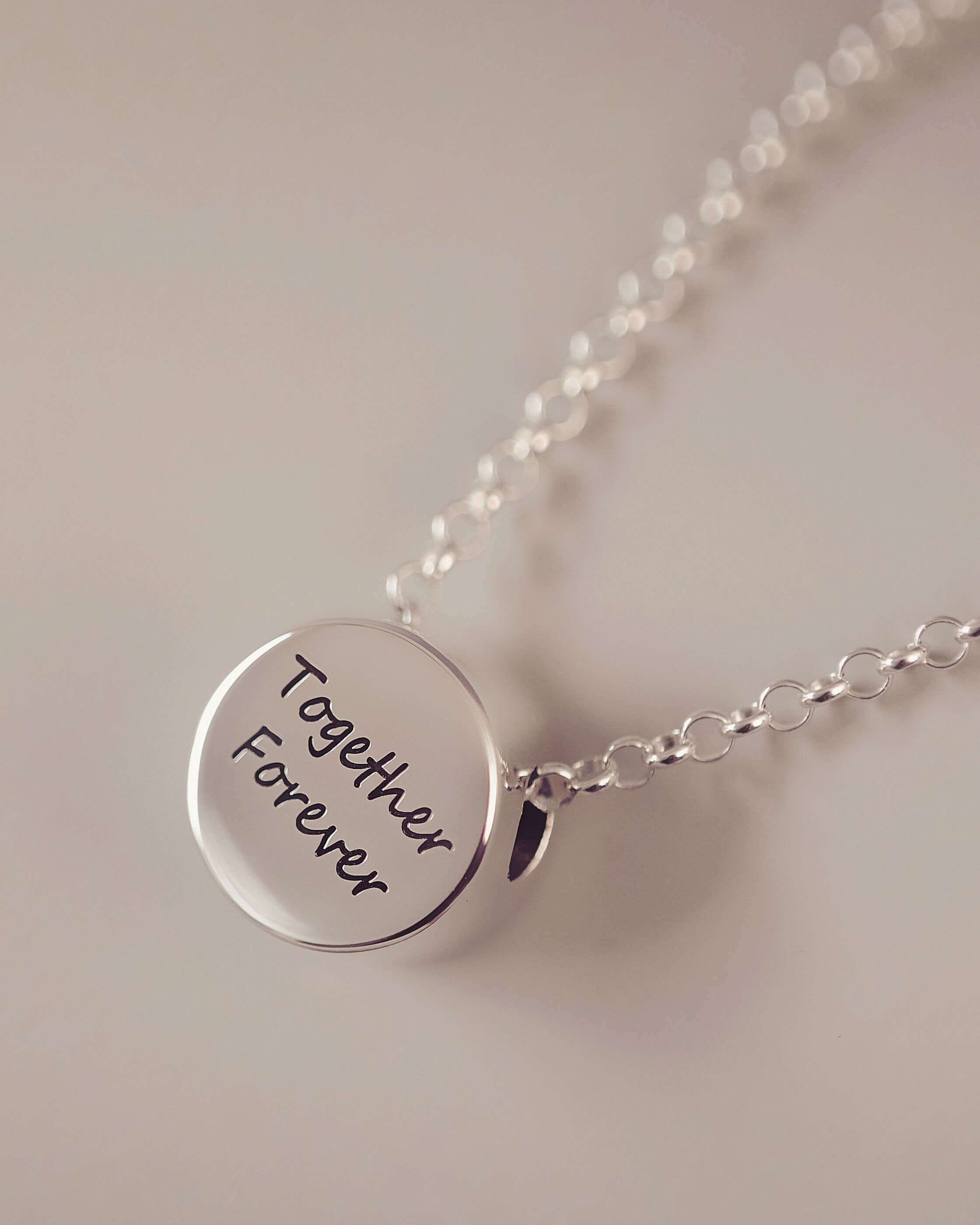 Silver necklace with a round pendant inscribed 'Together Forever' on a light background