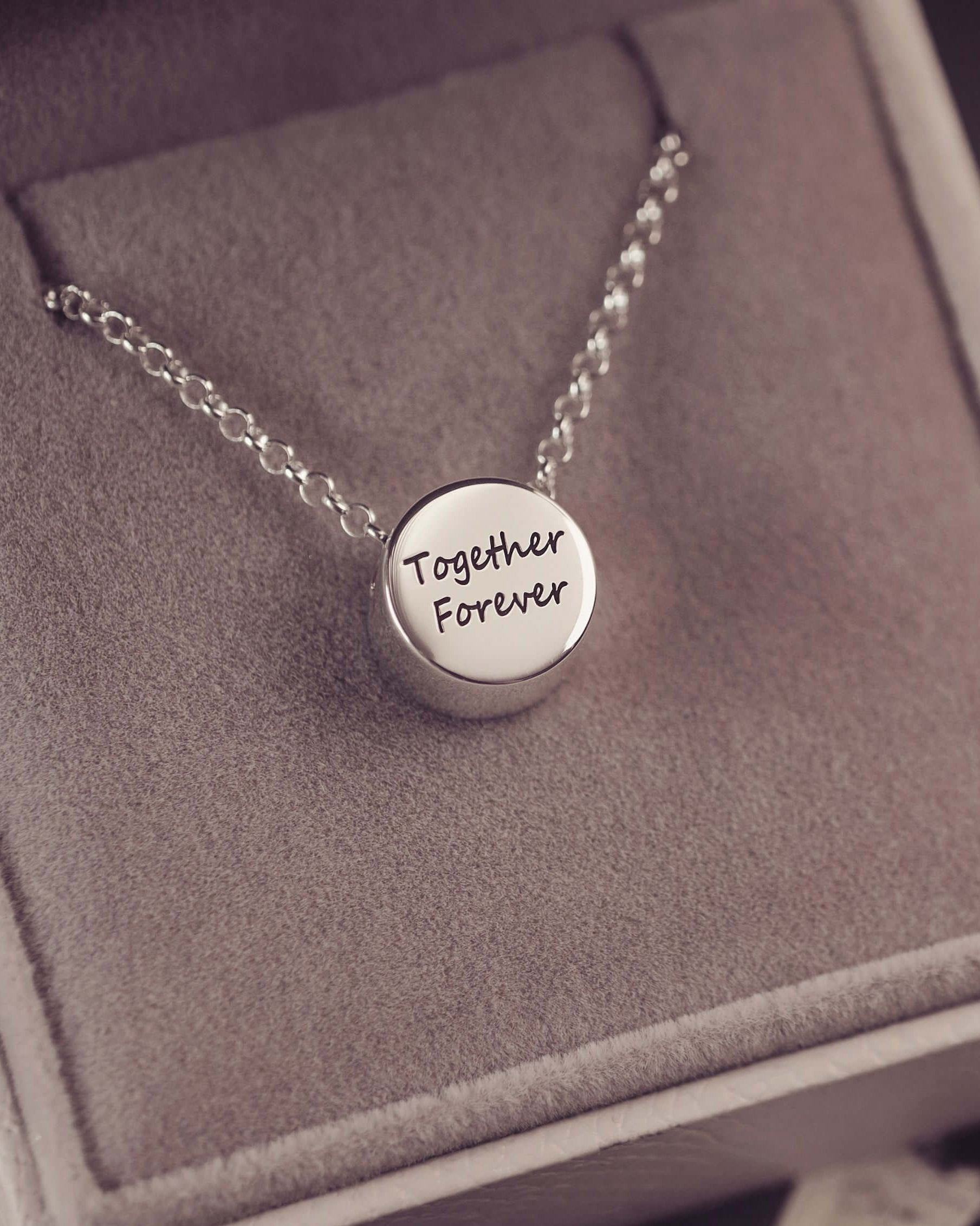Silver necklace with 'Together Forever' pendant on a gray box
