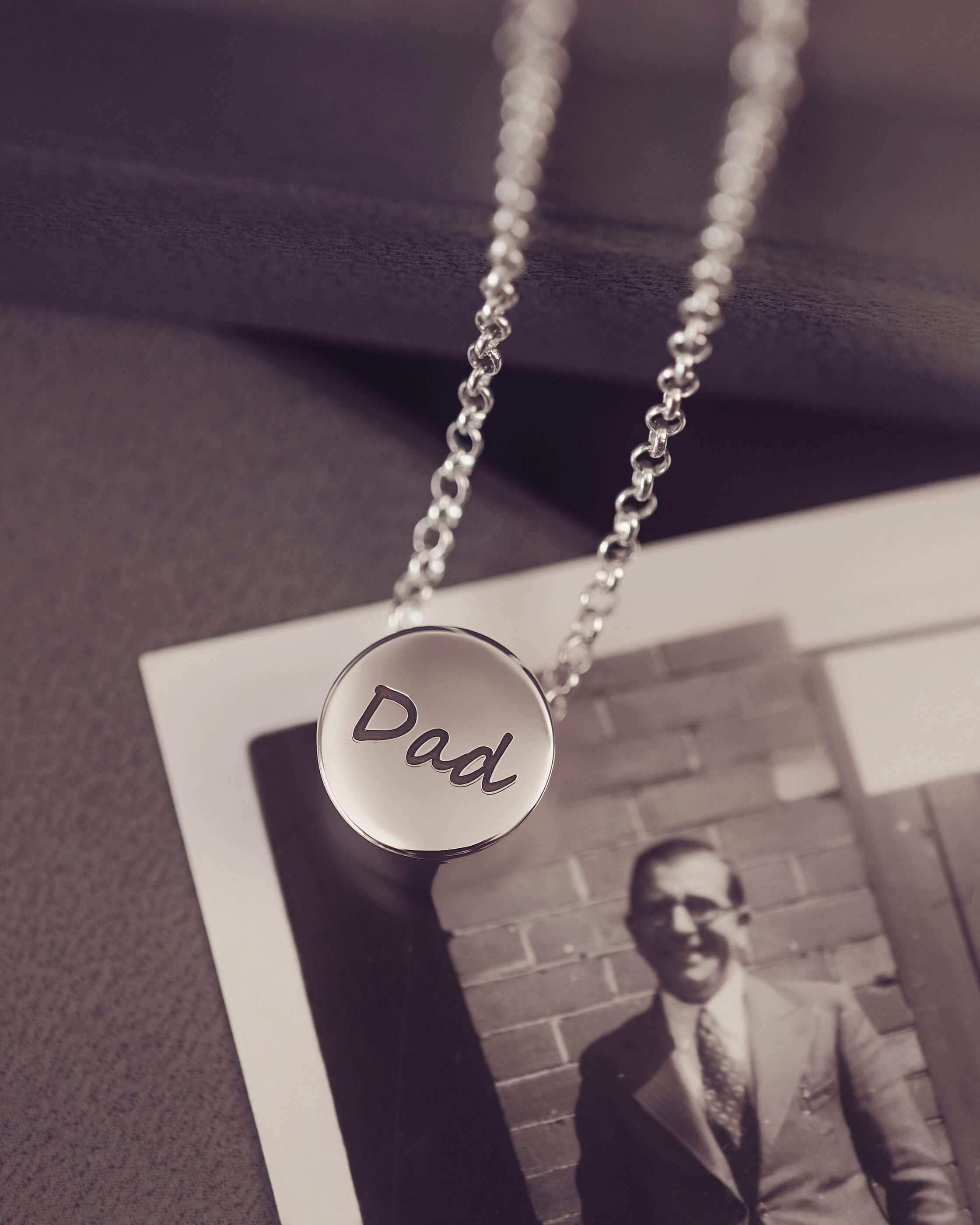 Silver necklace with 'Dad' pendant on a vintage photo background