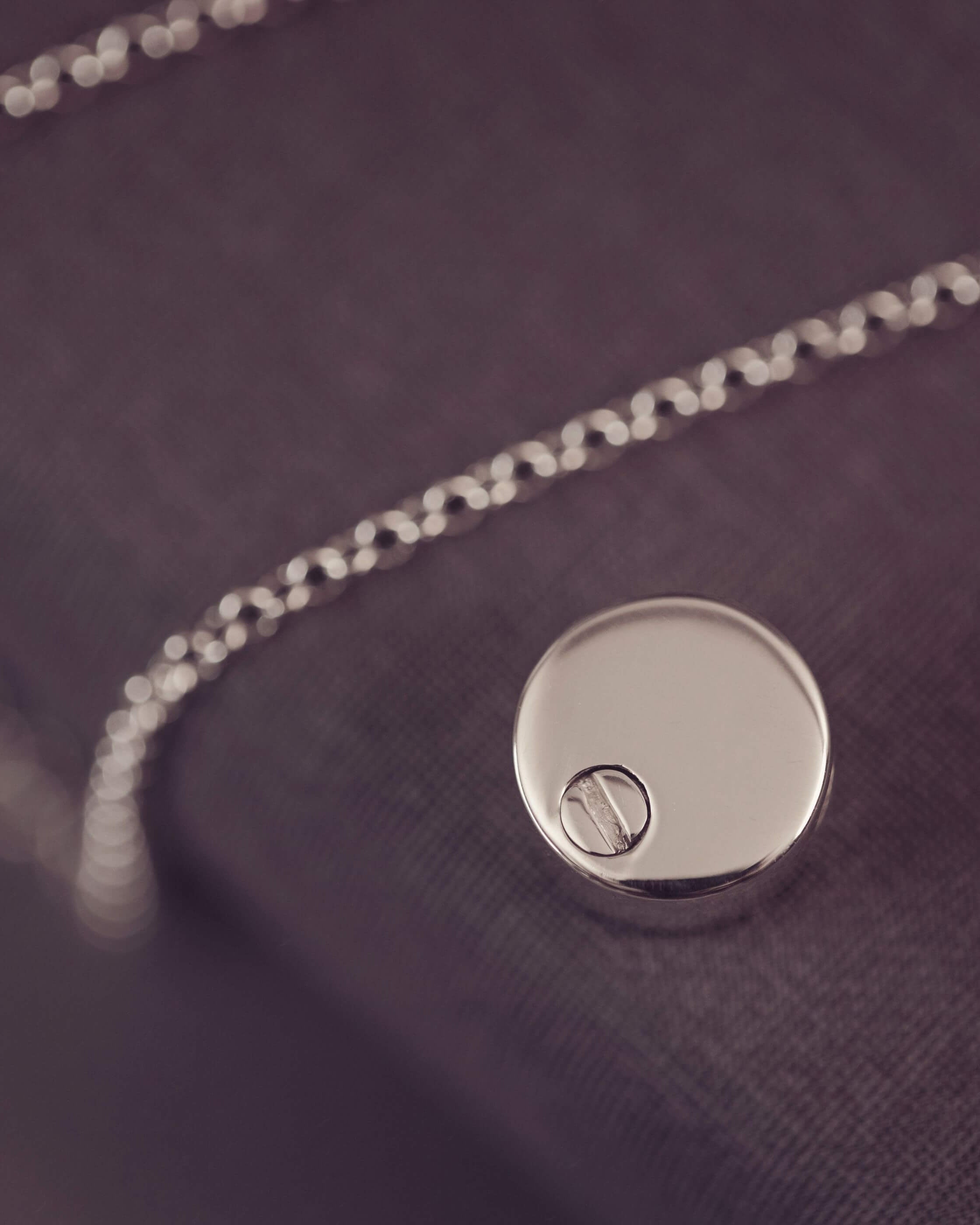 Close-up of a silver necklace with a round pendant on a dark fabric background