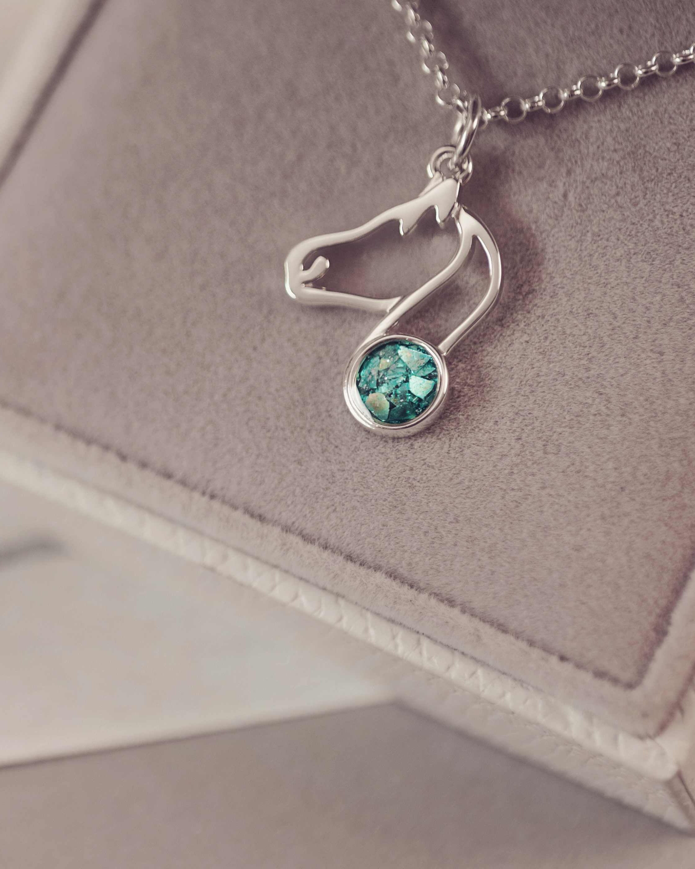 A silver shaped horse charm with green gemstone on a purple background