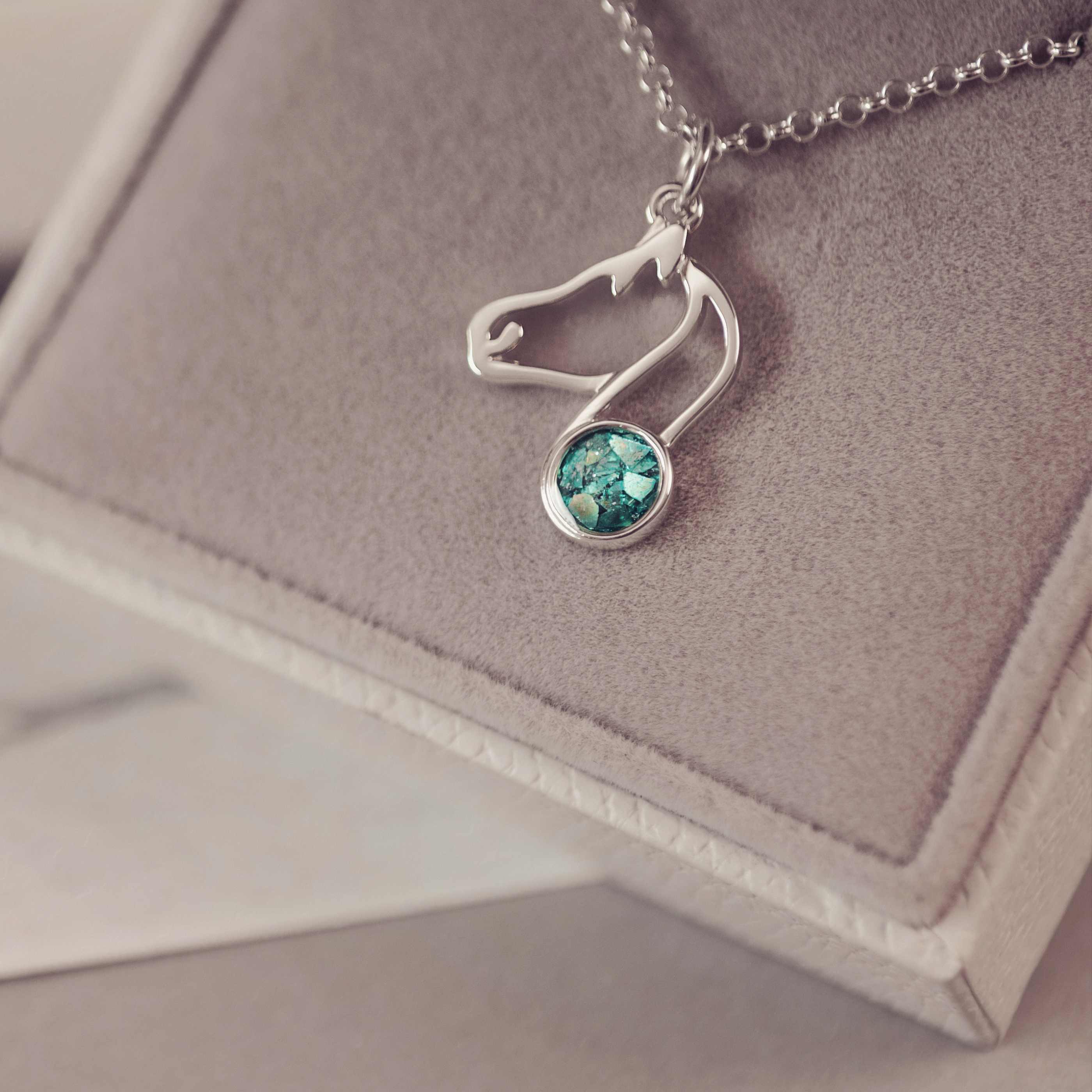 A silver shaped horse charm with green gemstone on a purple background