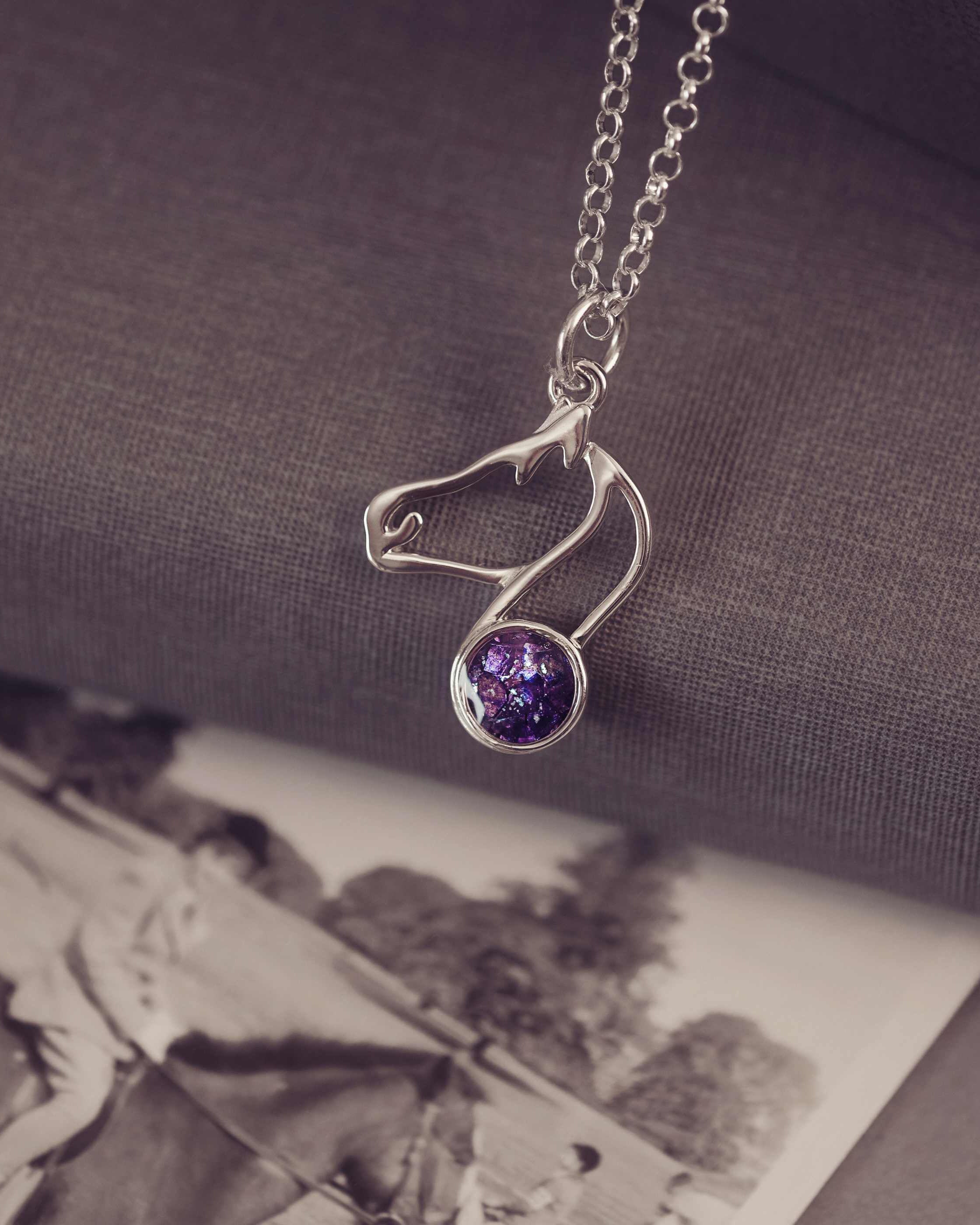 Silver necklace with a purple gemstone pendant on a textured surface with an old photograph underneath.