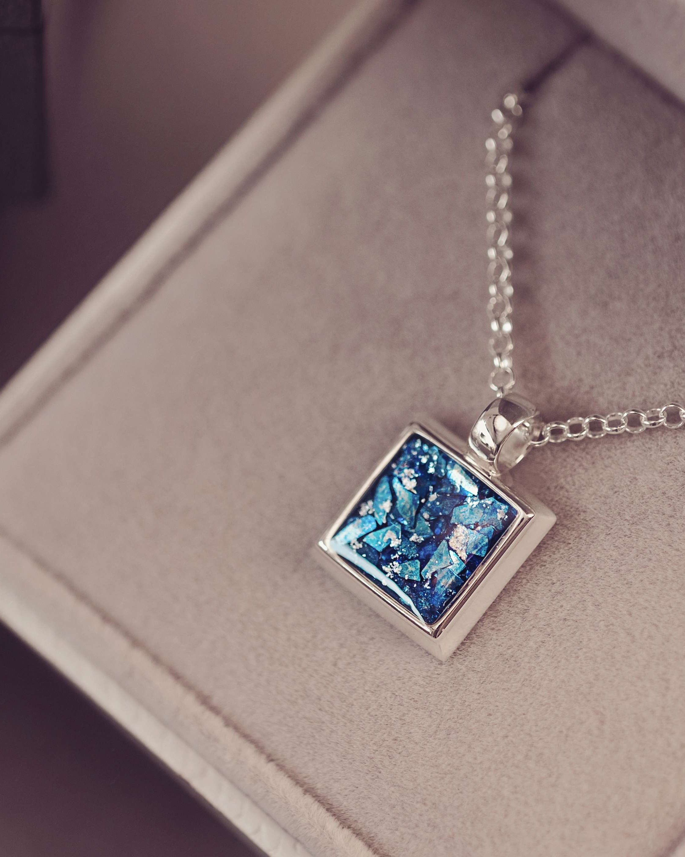 A silver square necklace filled with clue ashes and gemstones
