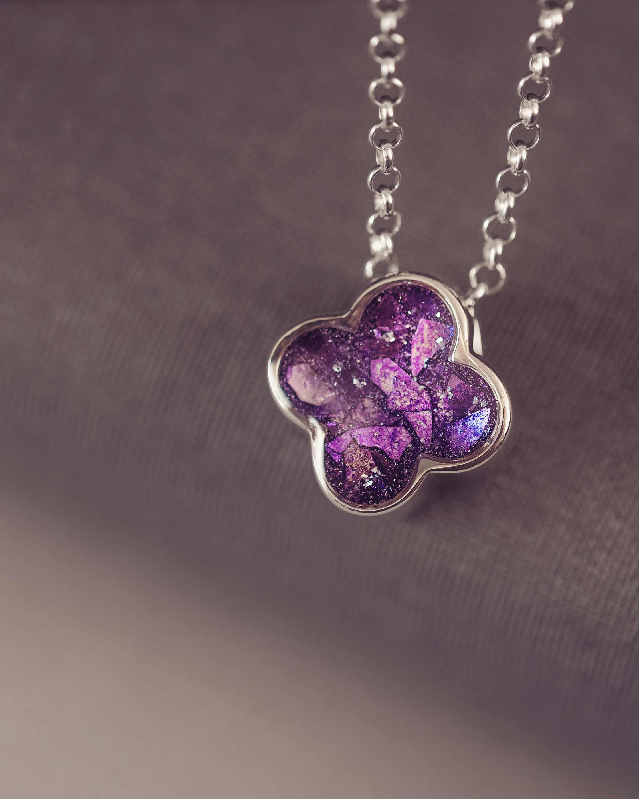 Purple flower-shaped pendant on a chain against a dark background