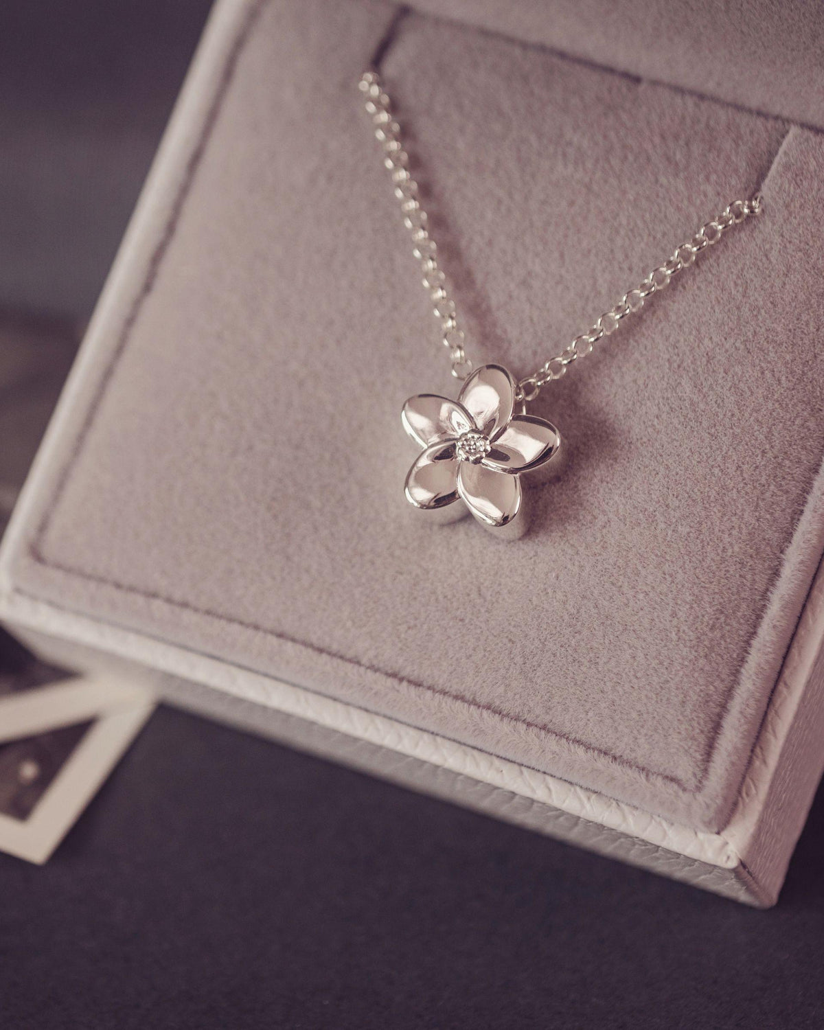 A silver flower pendant necklace resting on a gray velvet jewelry box.
