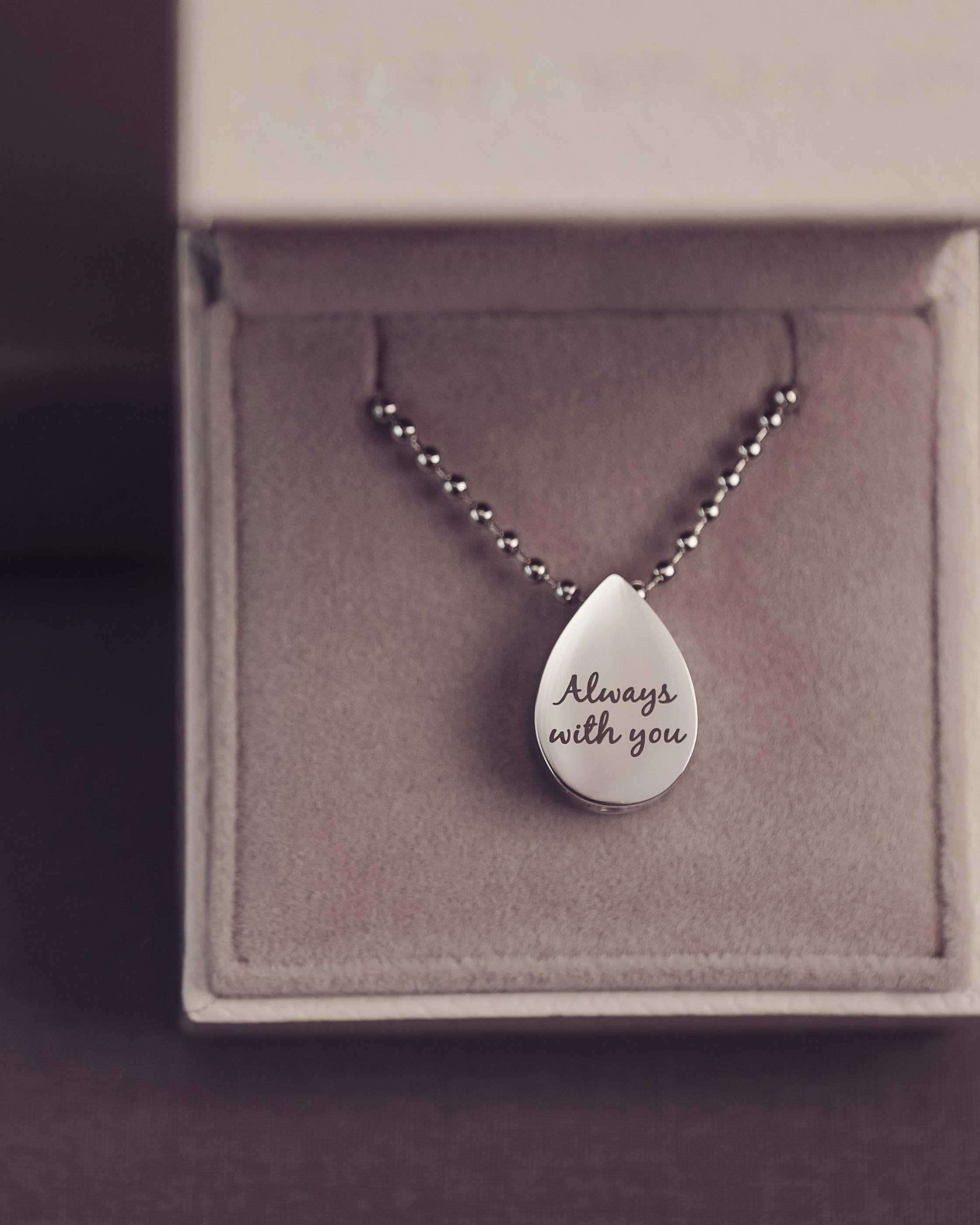 Silver teardrop pendant necklace with 'Always with you' engraving on a gray box.