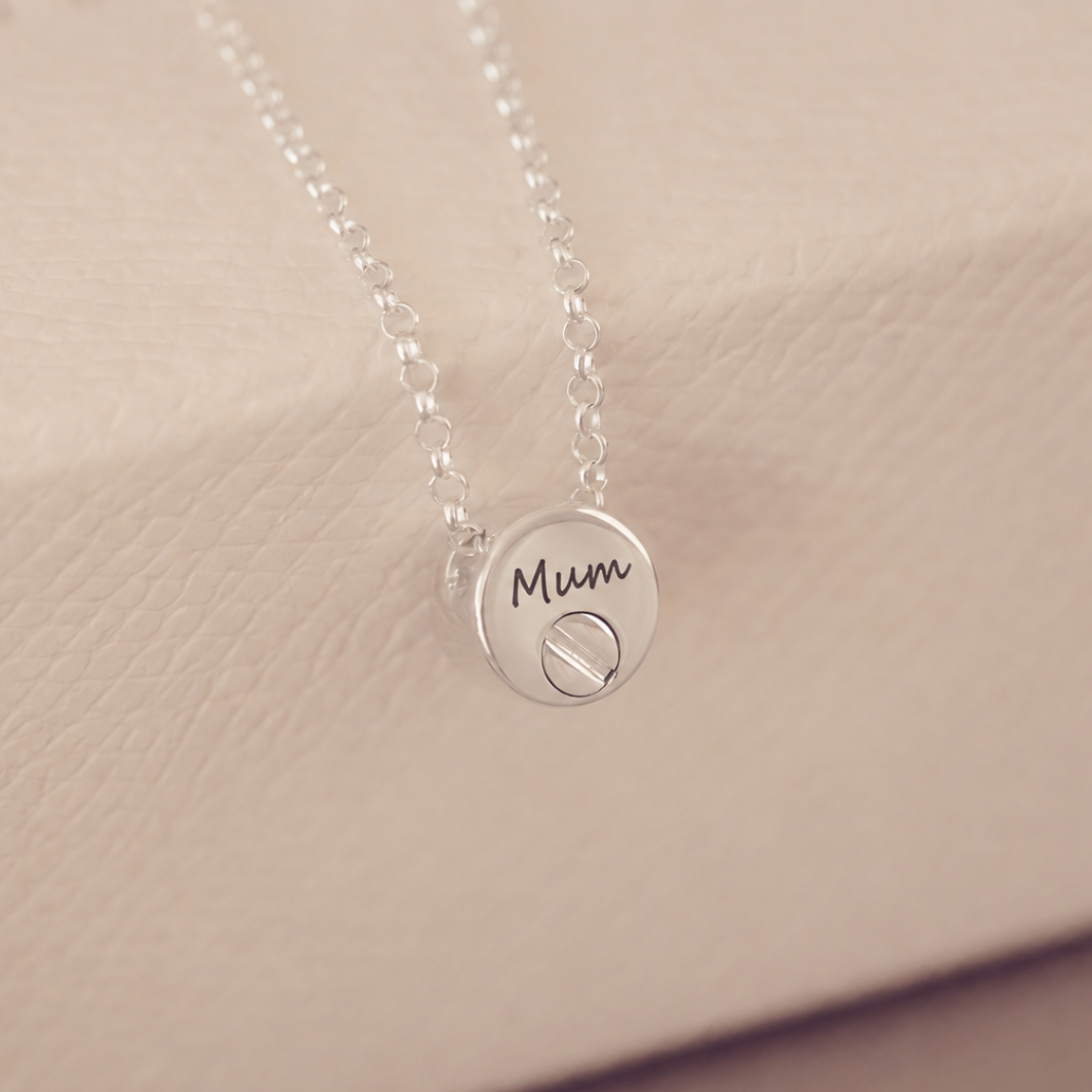 Silver necklace with a round pendant on a beige background, engraved with the word "Mum".