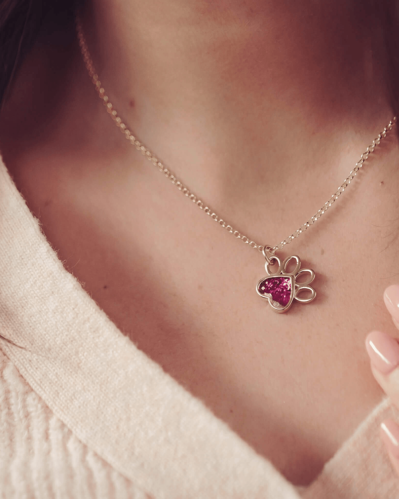 Woman in a jumper wearing a gold pawprint shaped necklace, with pink gem setting