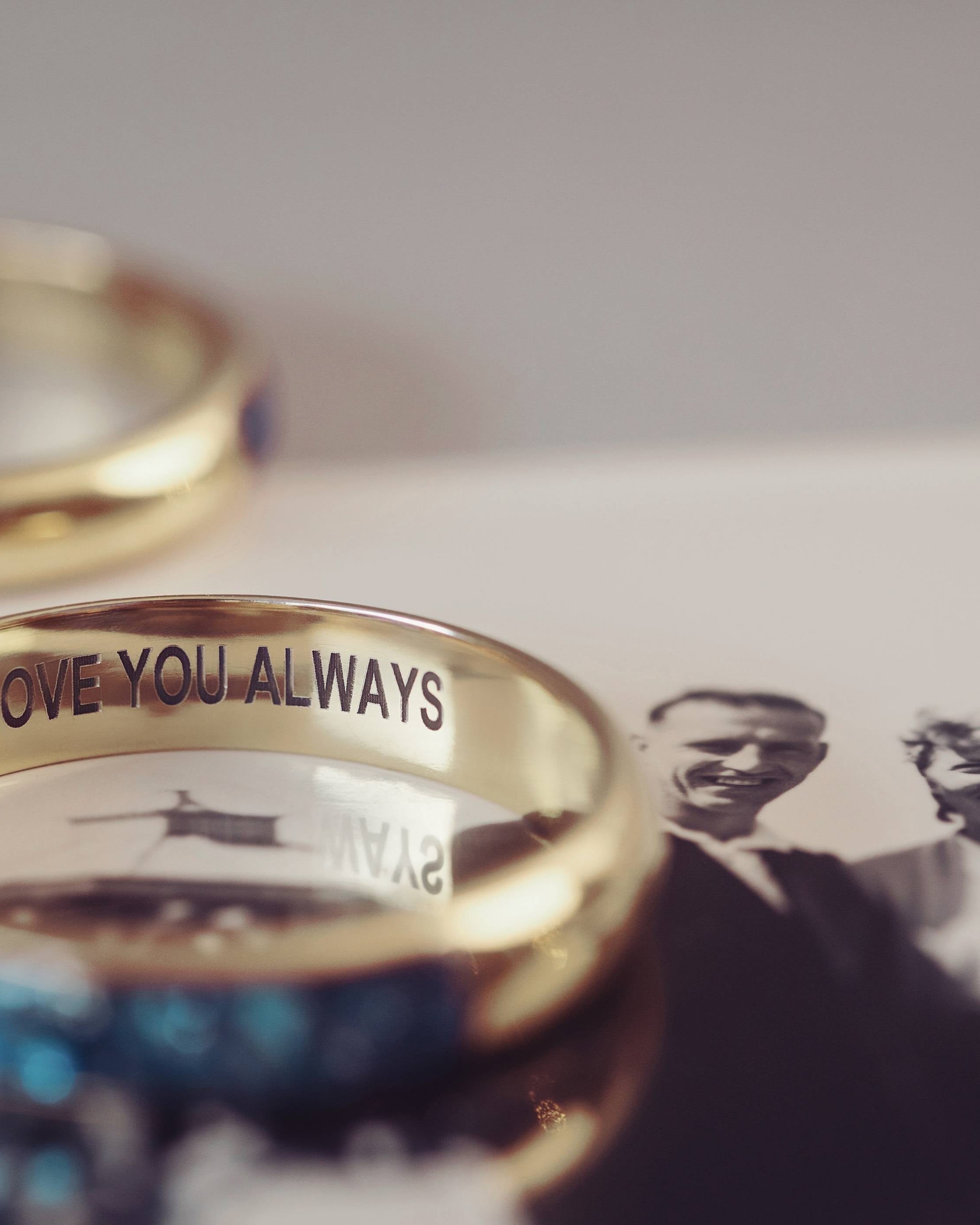 A gold ring with 'love you always' engraved. The ring is sitting on a black and white photograph of a man and lady.