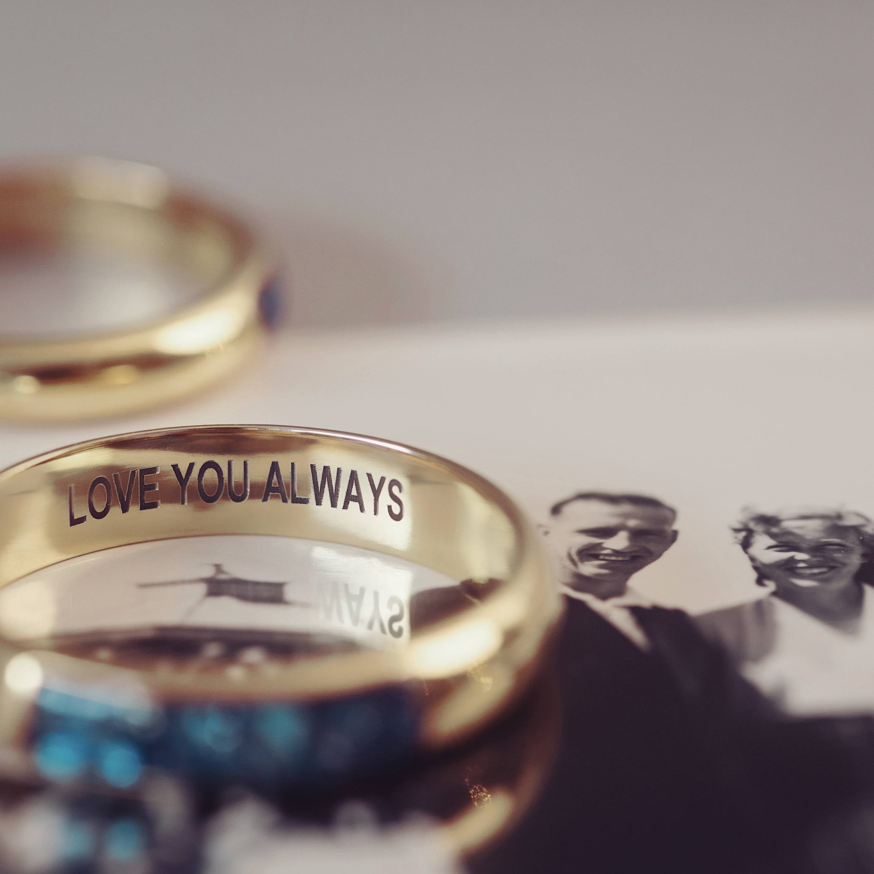 A gold ring with 'love you always' engraved. The ring is sitting on a black and white photograph of a man and lady.