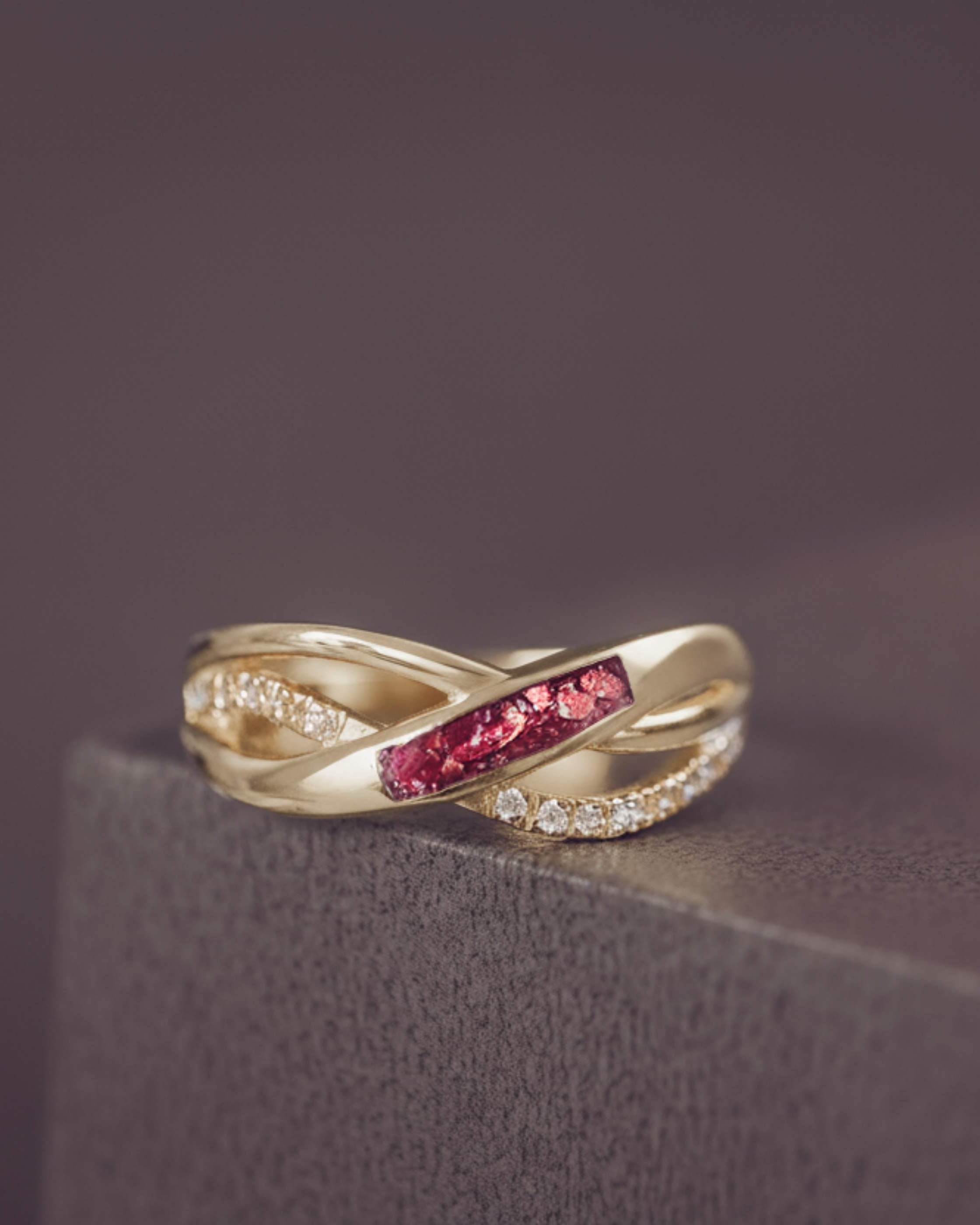 Gold ring with red gemstone and diamond accents on a dark surface