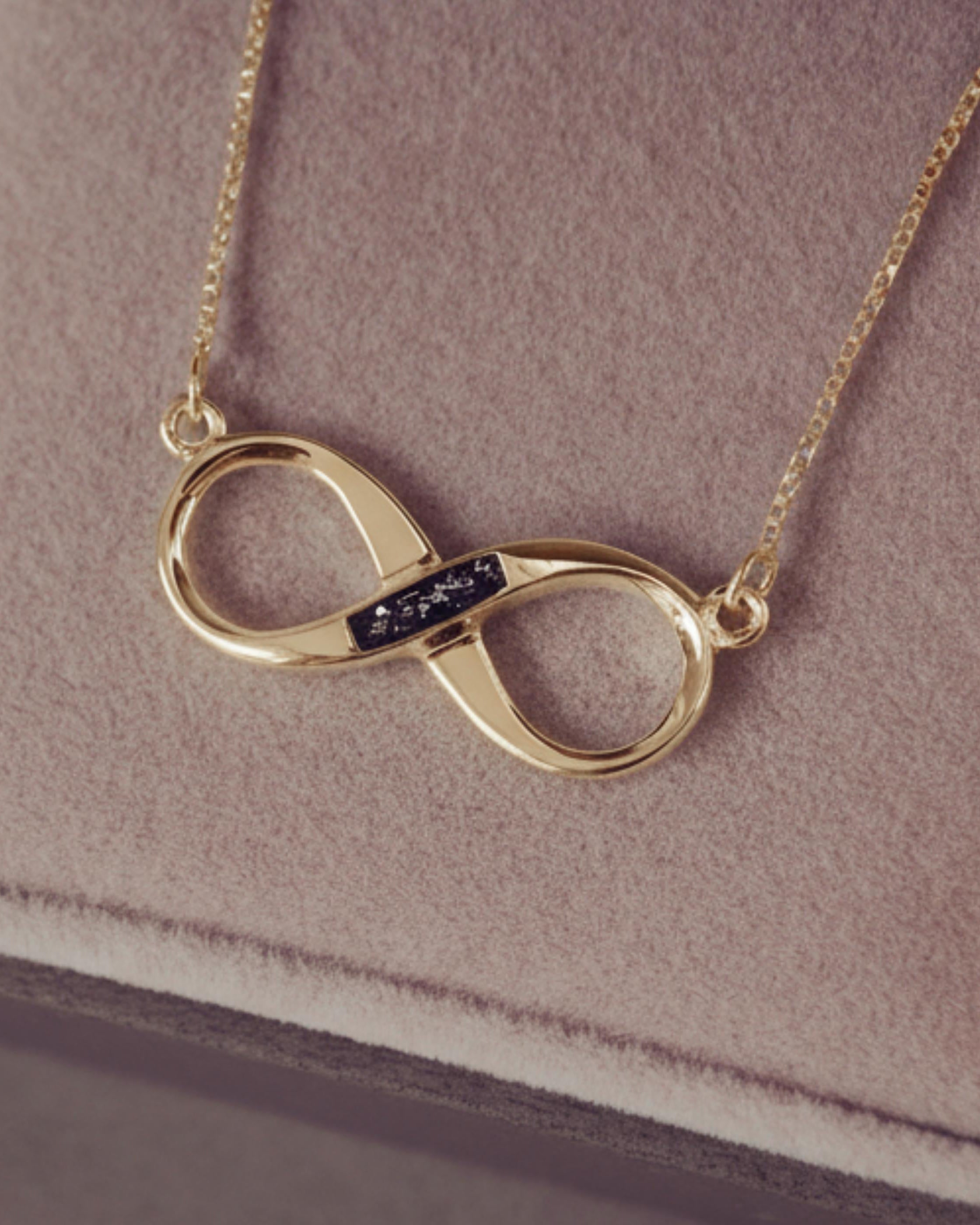 Gold infinity necklace on a soft pink background