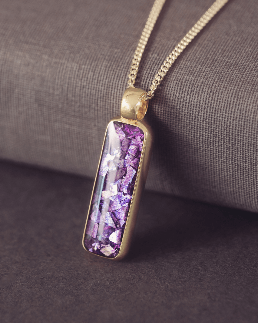 Gold necklace with a purple pendant on a textured surface