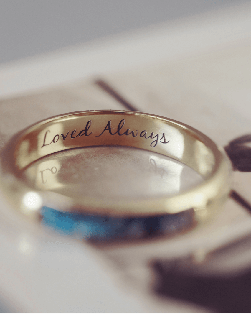 A gold ring with 'loved always' engraved. The ring is sitting on a black and white blurred photograph.